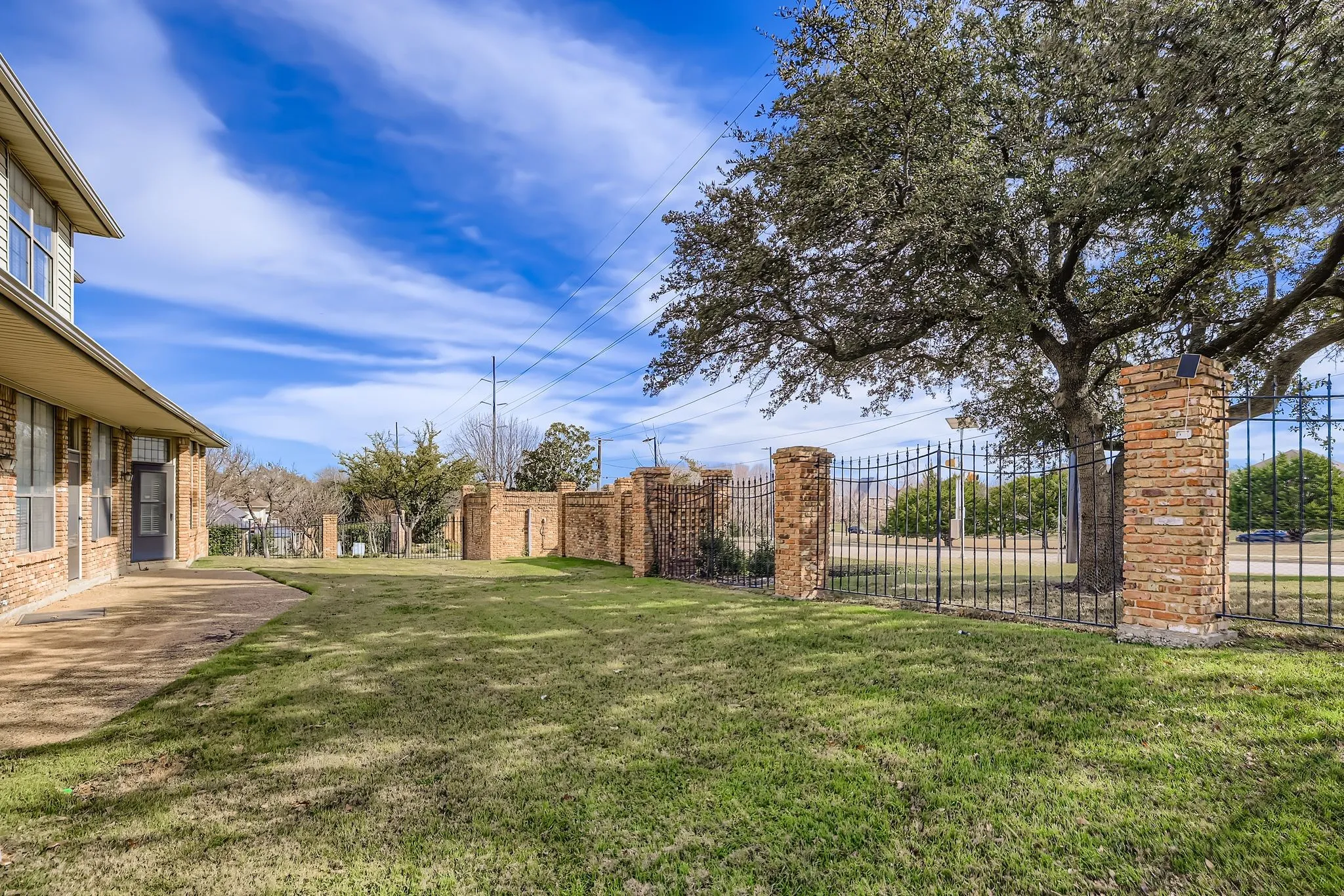 Expansive backyard featuring a manicured lawn, a paved patio, and a brick and wrought iron fence