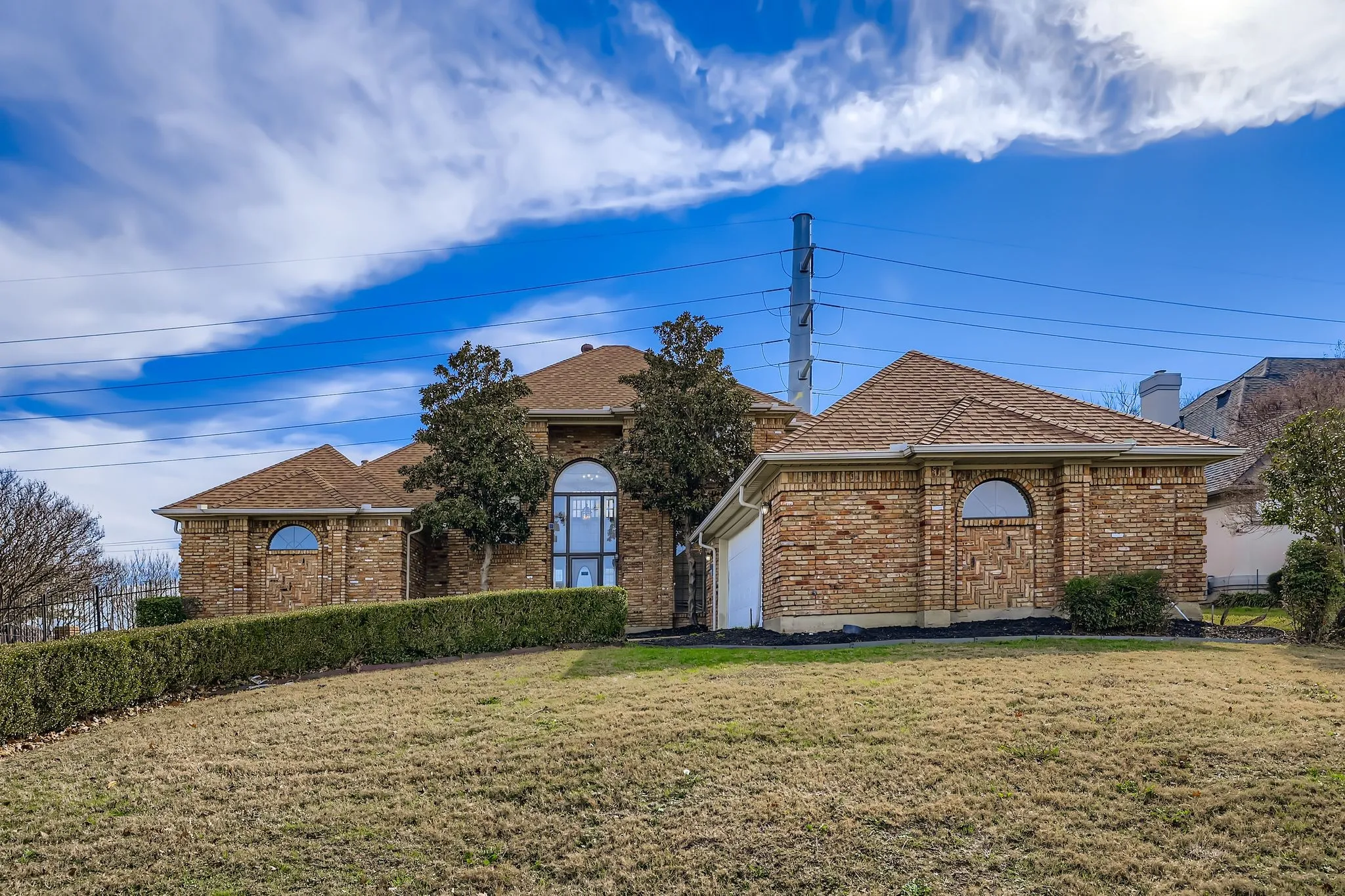 Brick exterior with multiple arched windows, mature landscaping, and an attached garage