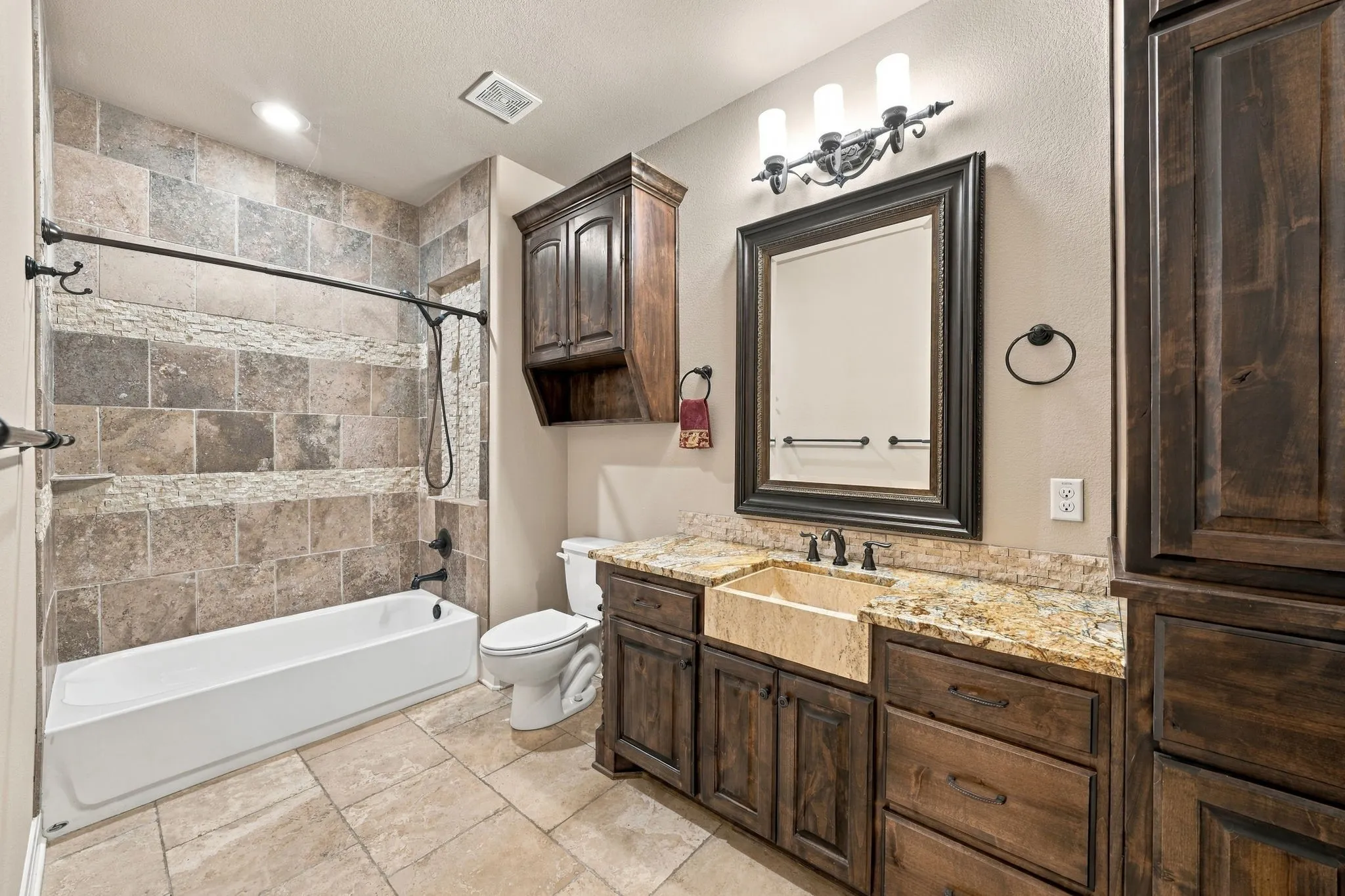 Bathroom featuring a white soaking tub, tiled shower surround, wood-finish vanity with a stone countertop, and a vessel sink