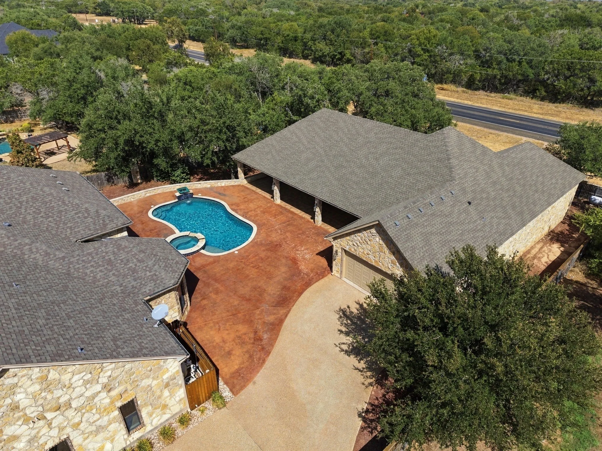 Freeform swimming pool with integrated spa and water feature, expansive stamped concrete patio, stone exterior, and attached garage