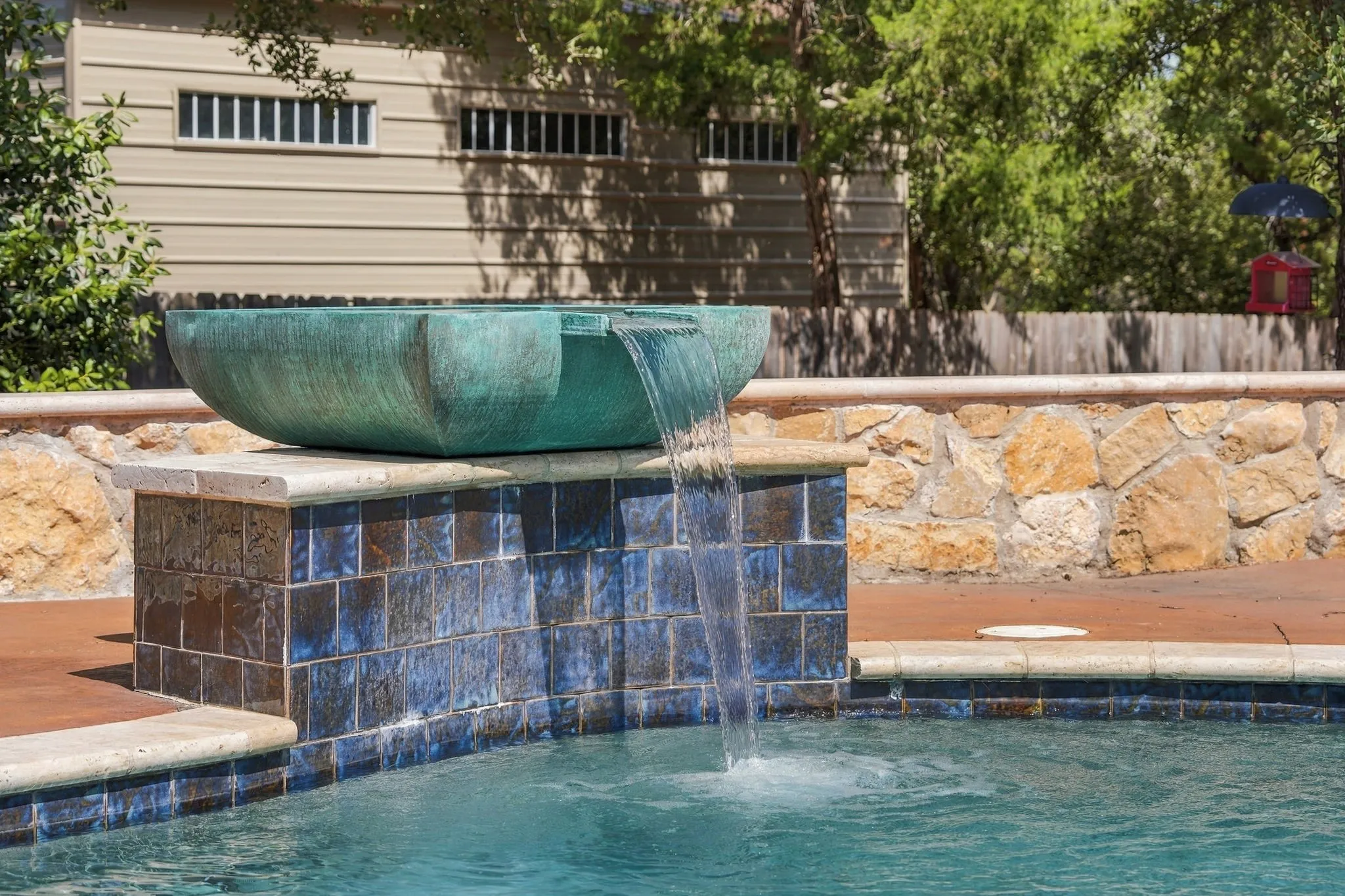 Pool water feature with a copper-toned basin, blue mosaic tile accents, and a stone-clad retaining wall
