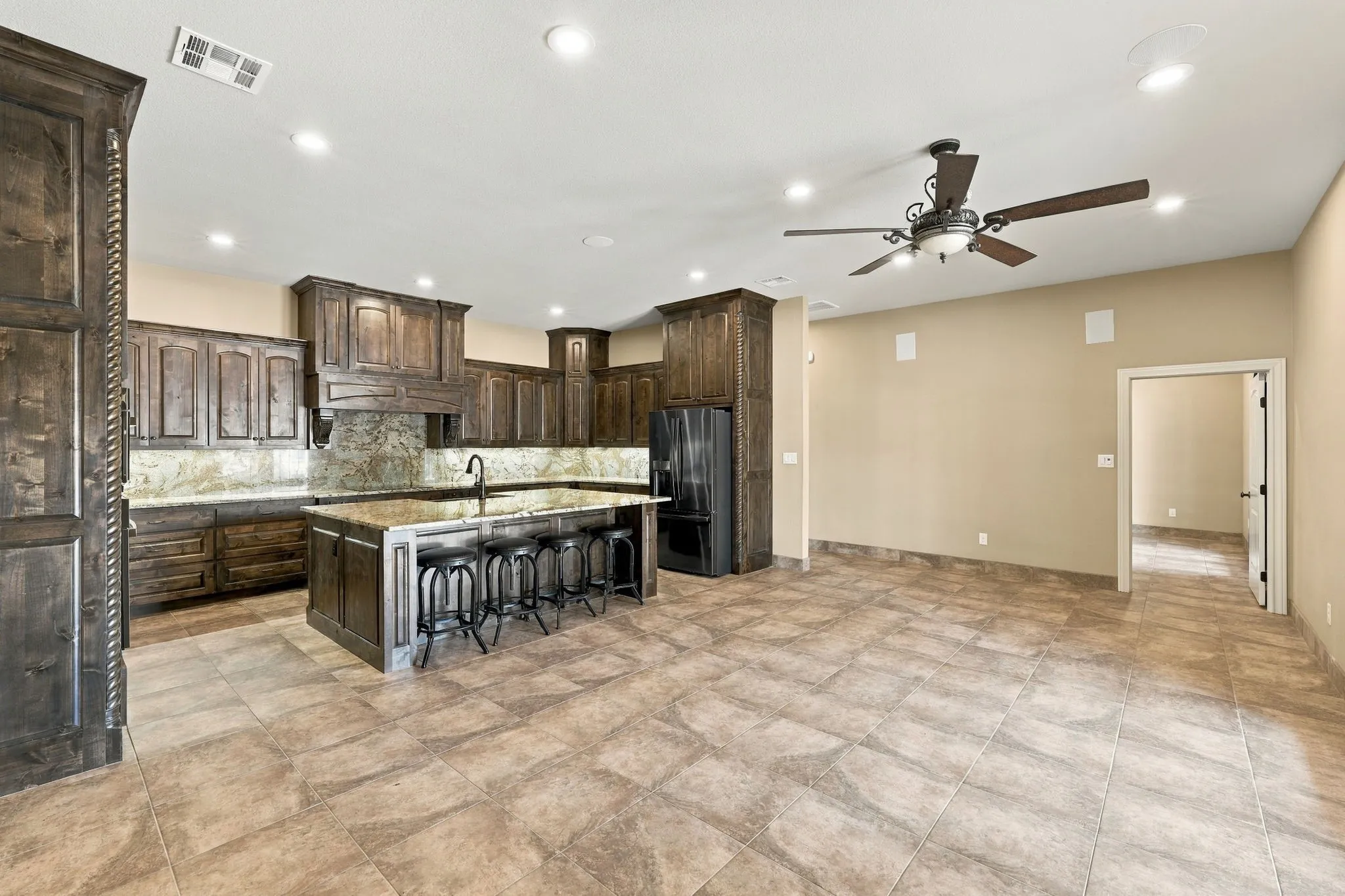 Spacious kitchen featuring extensive wood cabinetry, granite countertops, a large center island with seating, a built-in refrigerator, and ceiling-mounted lighting