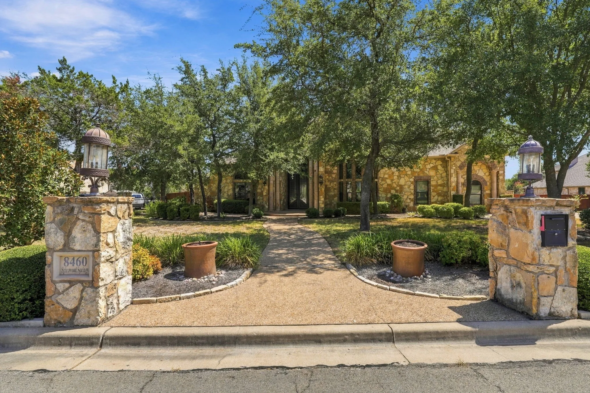 Stone-clad exterior, stone entry pillars with integrated lighting, exposed aggregate pathway, mature trees, and landscaping