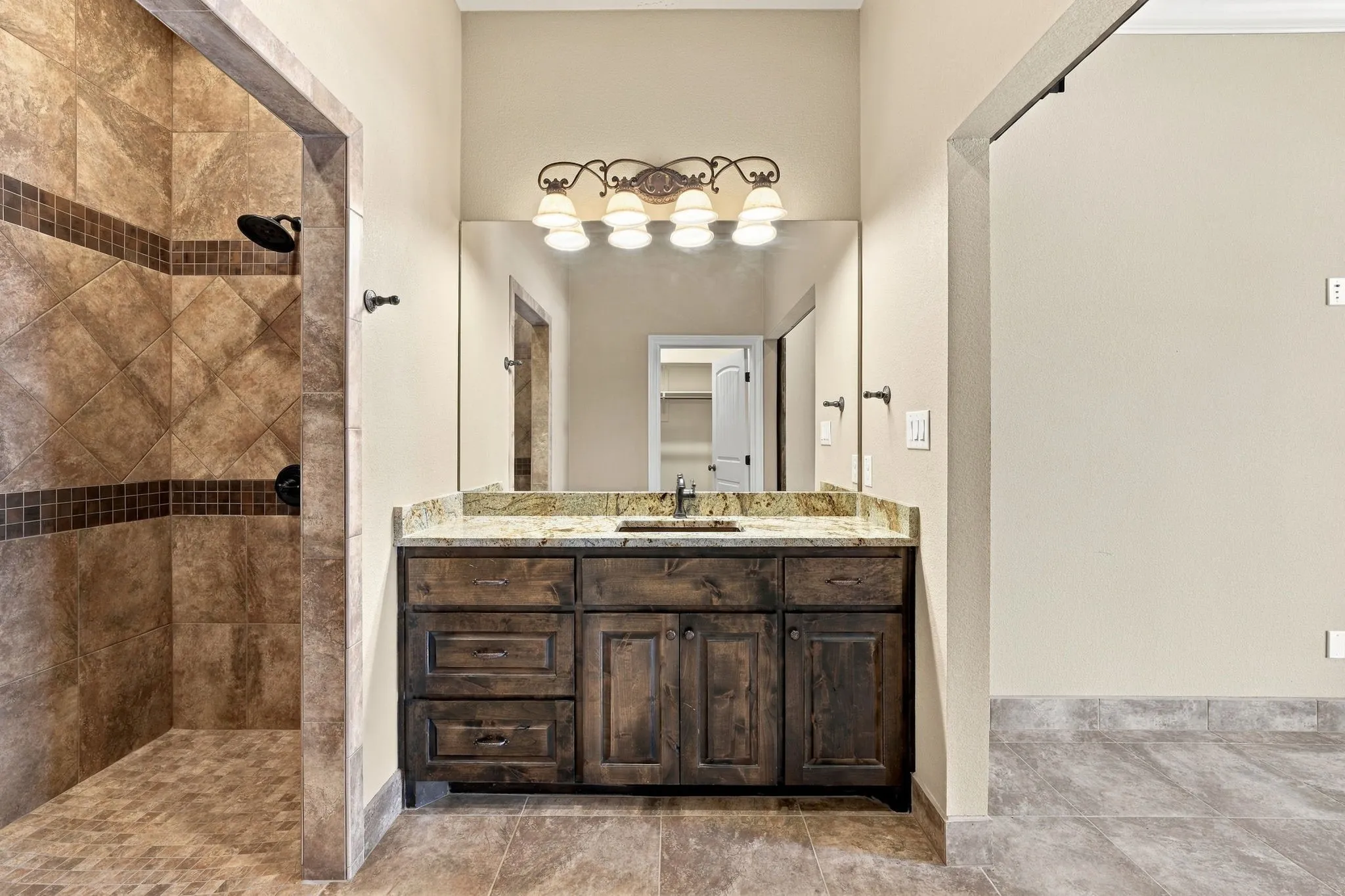 Walk-in shower with tiled walls and floor, vanity with wood-finish cabinetry, stone countertop, and an integrated sink, illuminated by a decorative light fixture