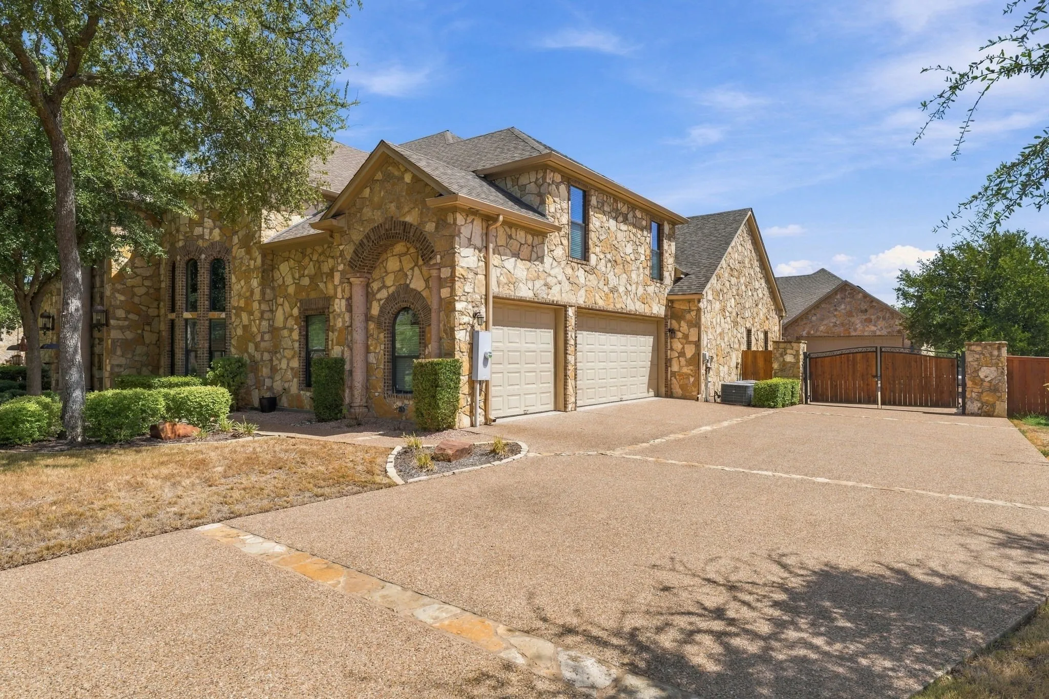 Stone exterior with arched entryways, multi-car garage, and a gated motor court