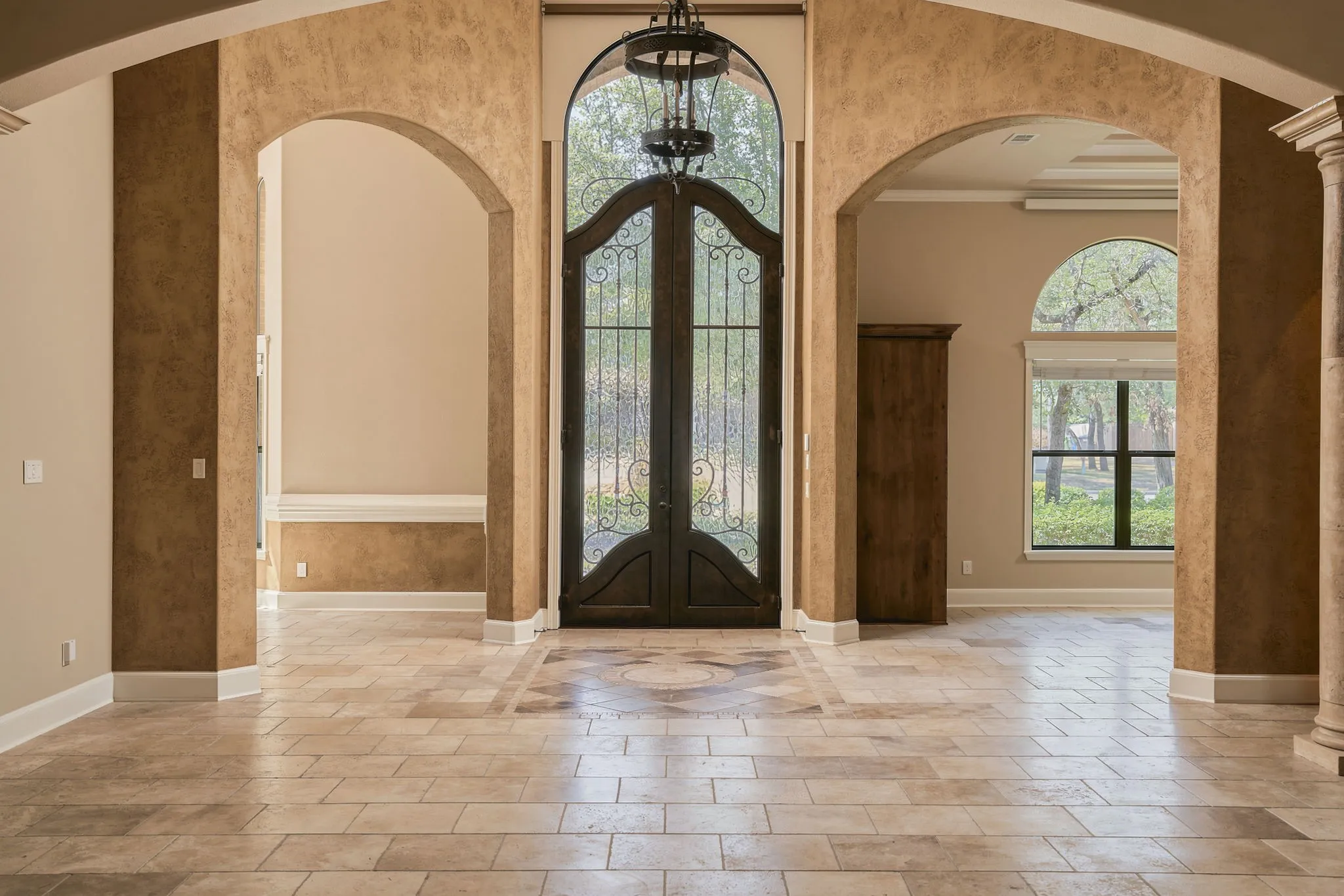 Arched entryways with textured wall finishes, tile flooring, wrought iron entry doors, and a built-in wooden cabinet