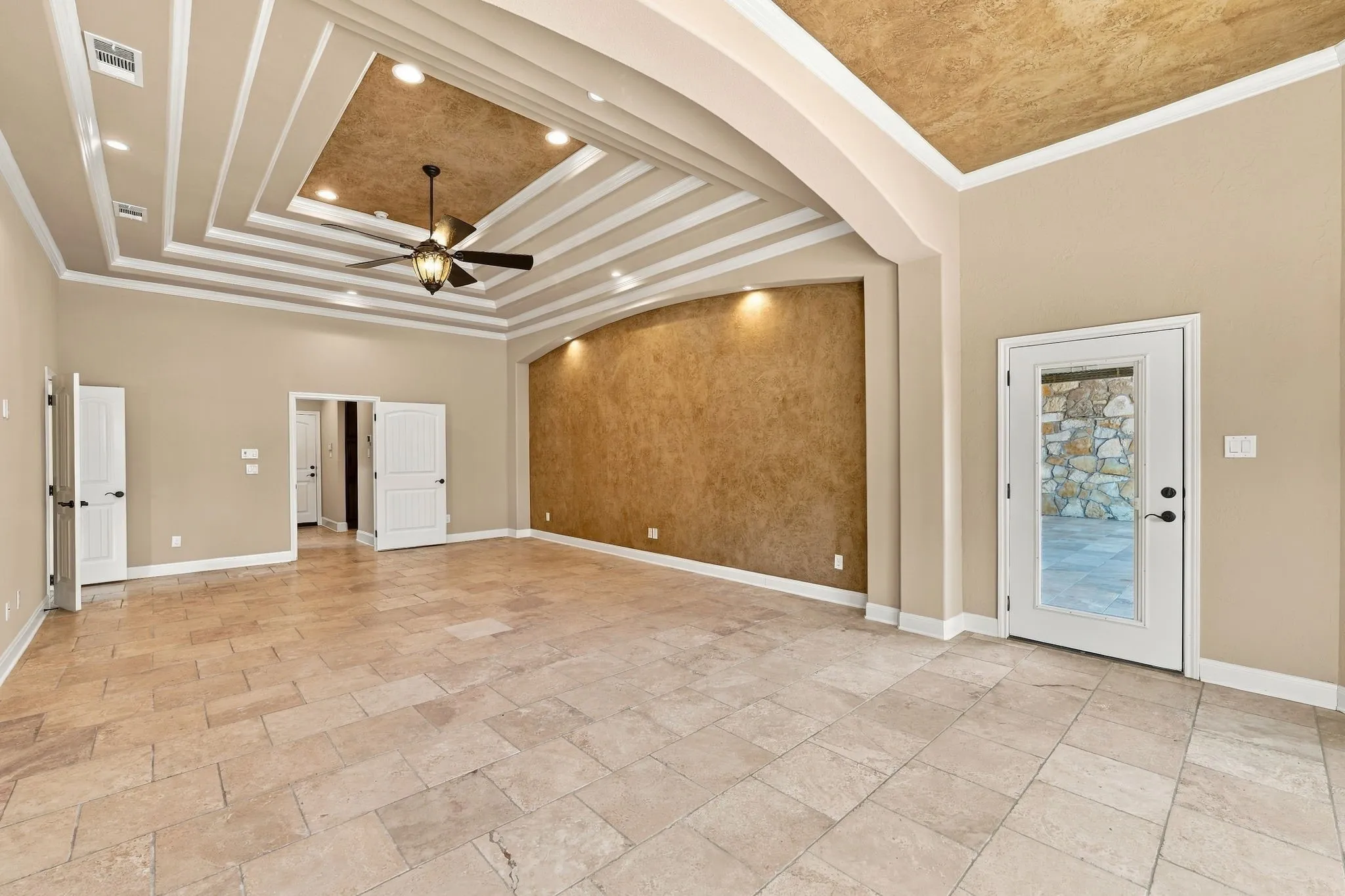 Recessed tray ceiling with crown molding, tiled flooring, arched doorway, and a ceiling fan
