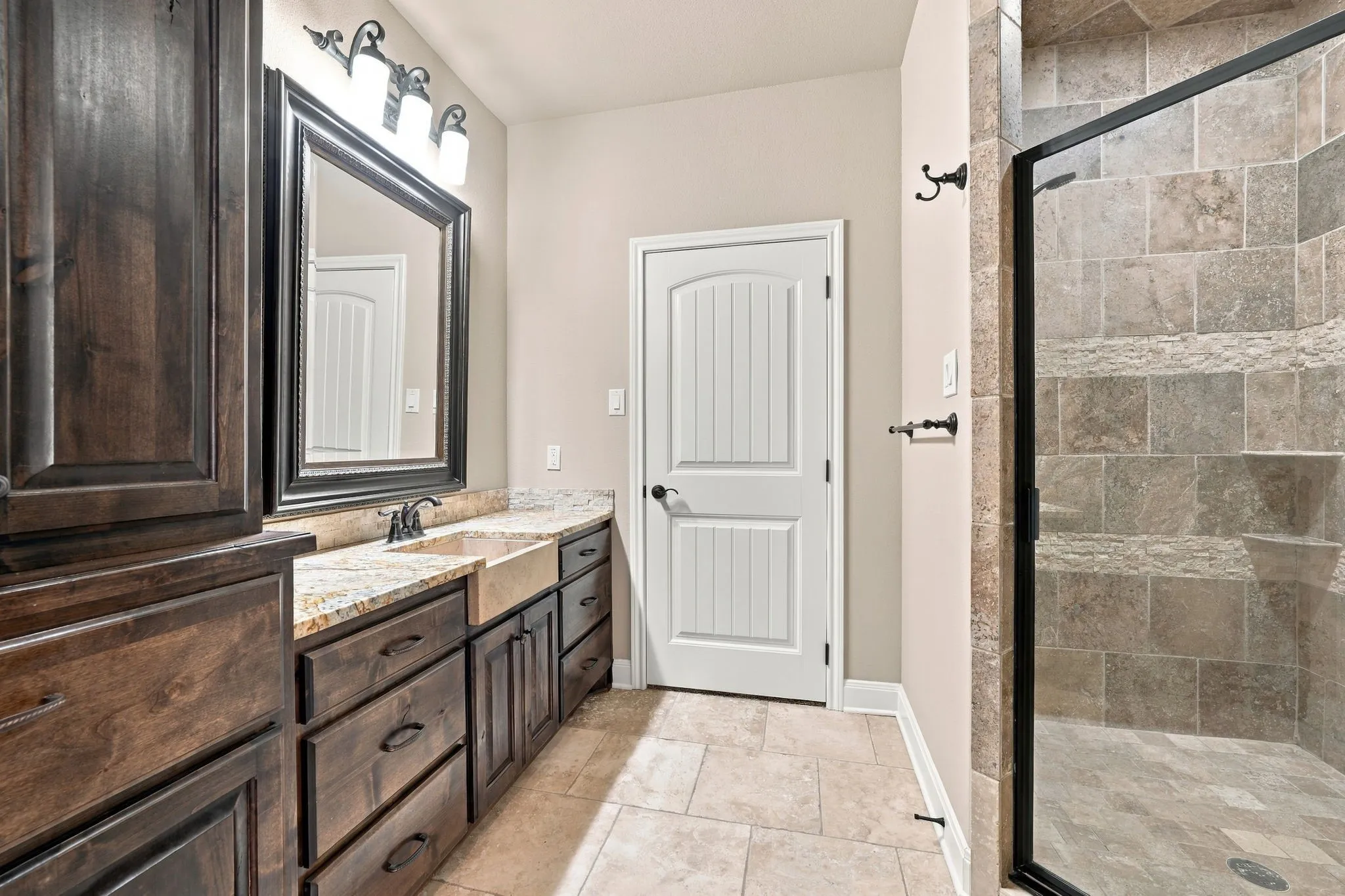 Dual vanity with integrated sinks, wood-finish cabinetry, stone-finish countertops, tiled flooring, and a tiled shower with a glass enclosure