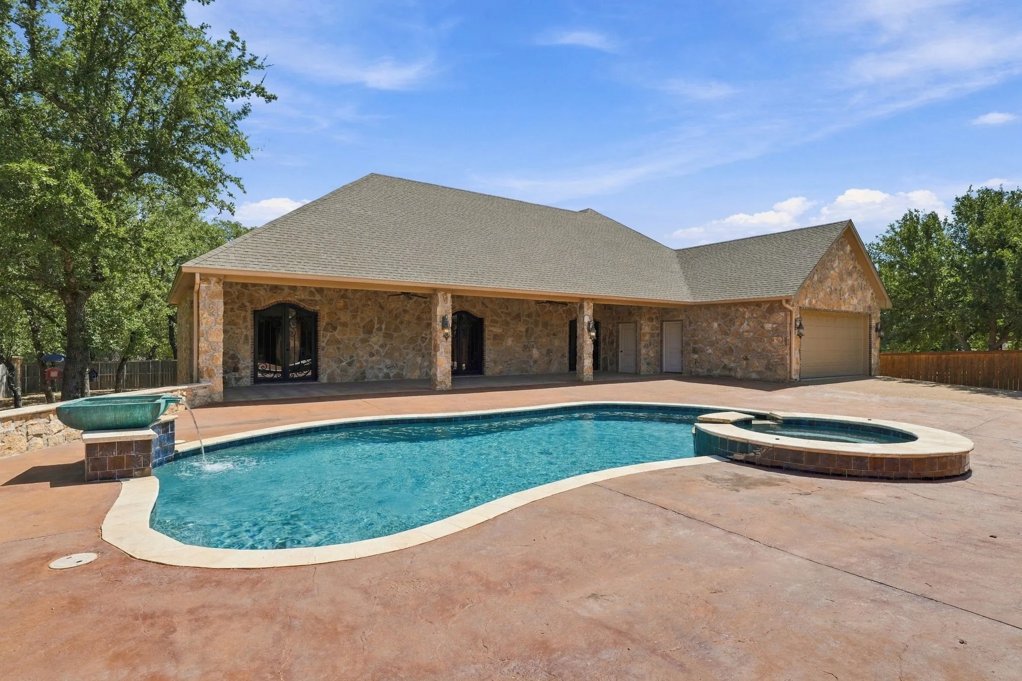 Stone veneer exterior with a covered patio, an integrated swimming pool, a circular spa, and an attached garage