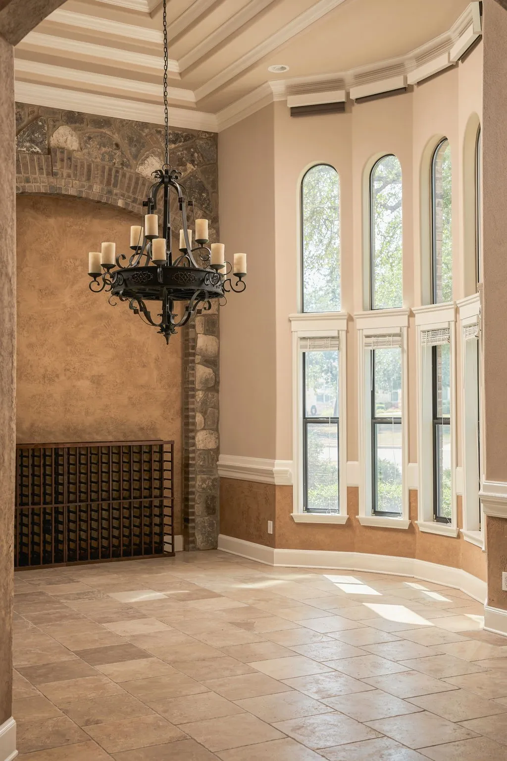 Bay window with arched upper panes, tile flooring, built-in wine rack, stone and stucco wall details, and a wrought iron chandelier