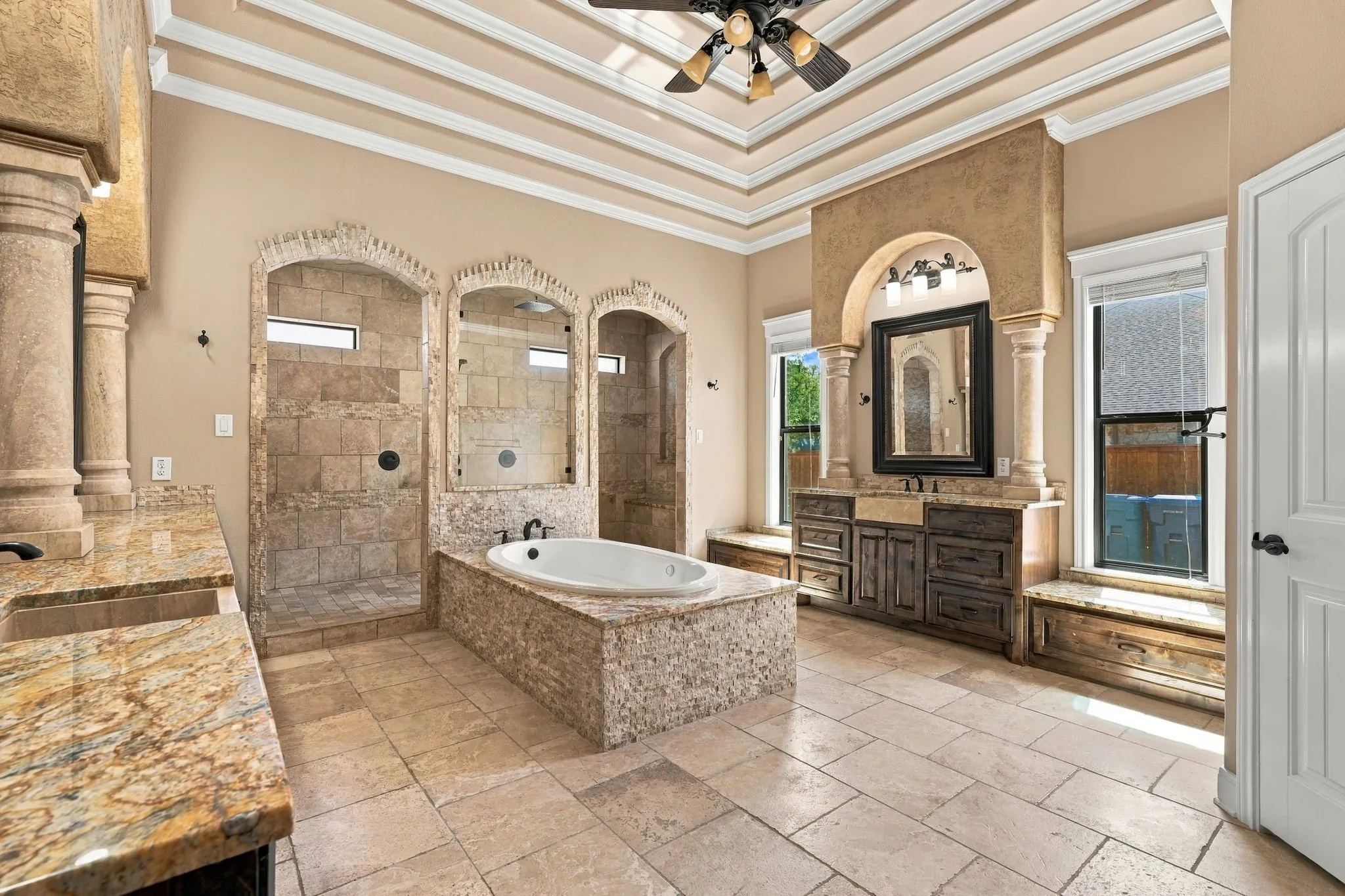 Coffered ceiling, dual stone vanities, built-in soaking tub, arched walk-in shower, and tile flooring