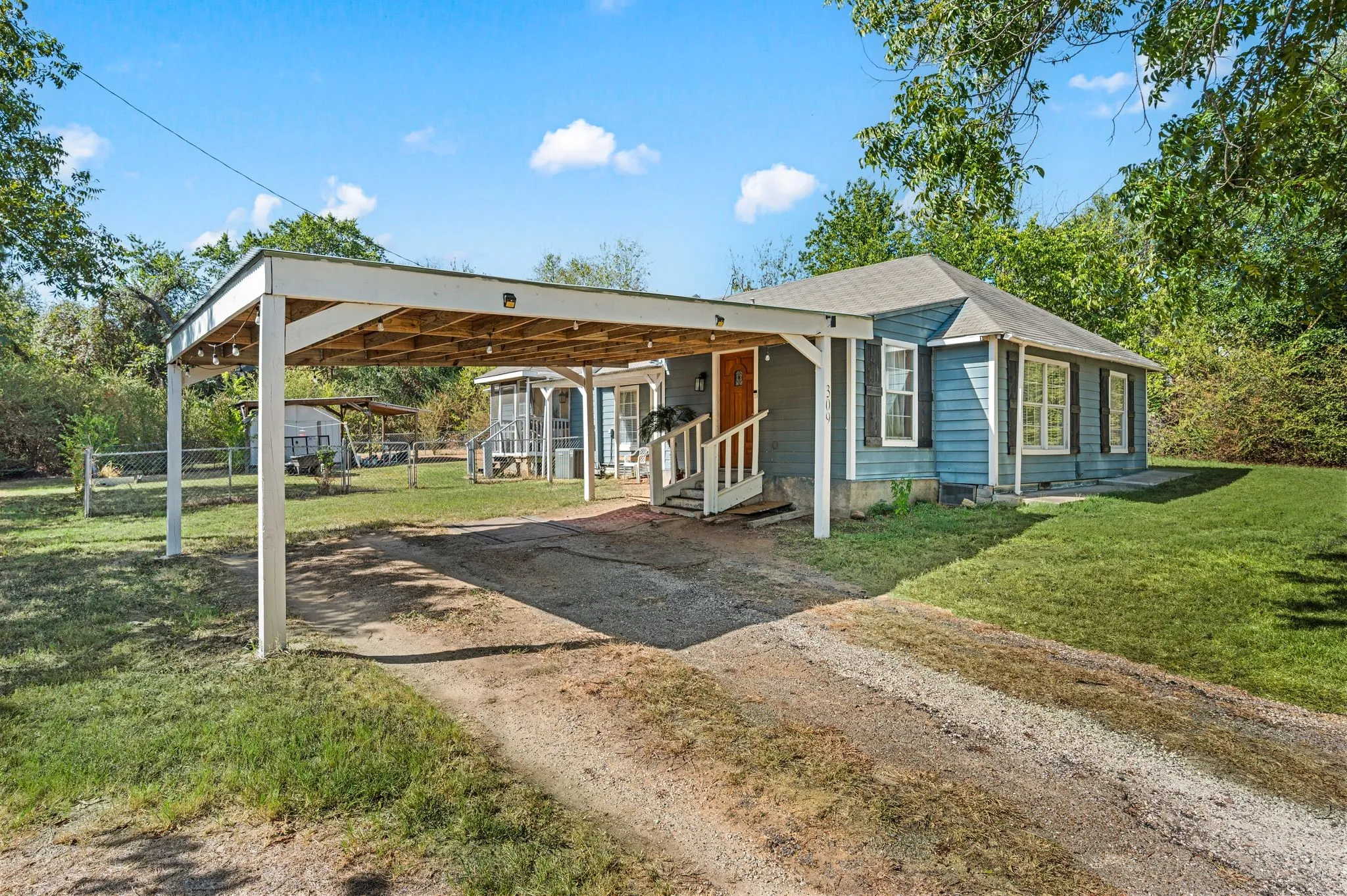 Carport structure, front porch with railing, blue siding, multiple windows with dark shutters, and a sloped roof