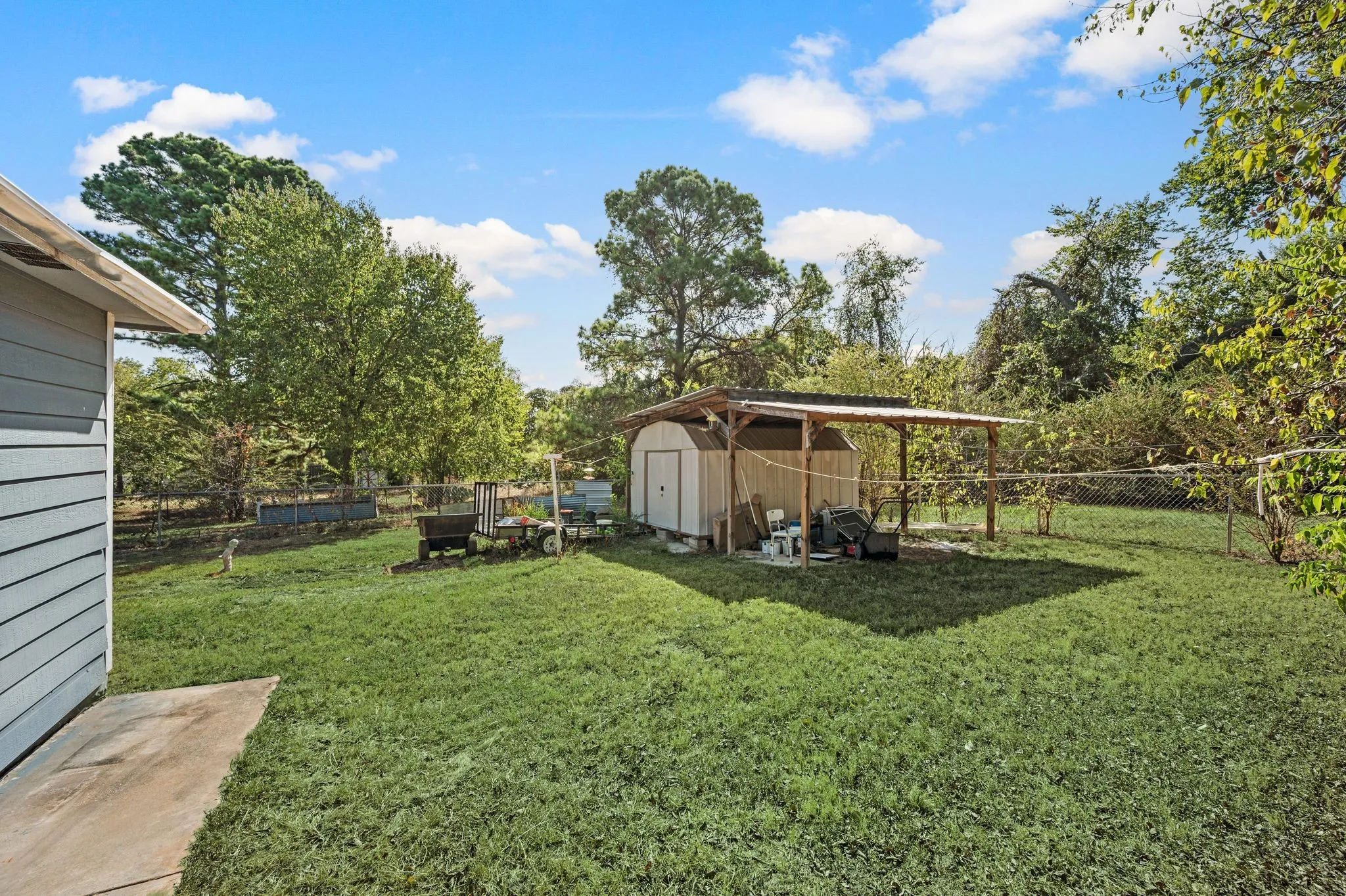 Expansive lawn area, chain link fencing, mature perimeter trees, and a detached shed with an attached covered structure