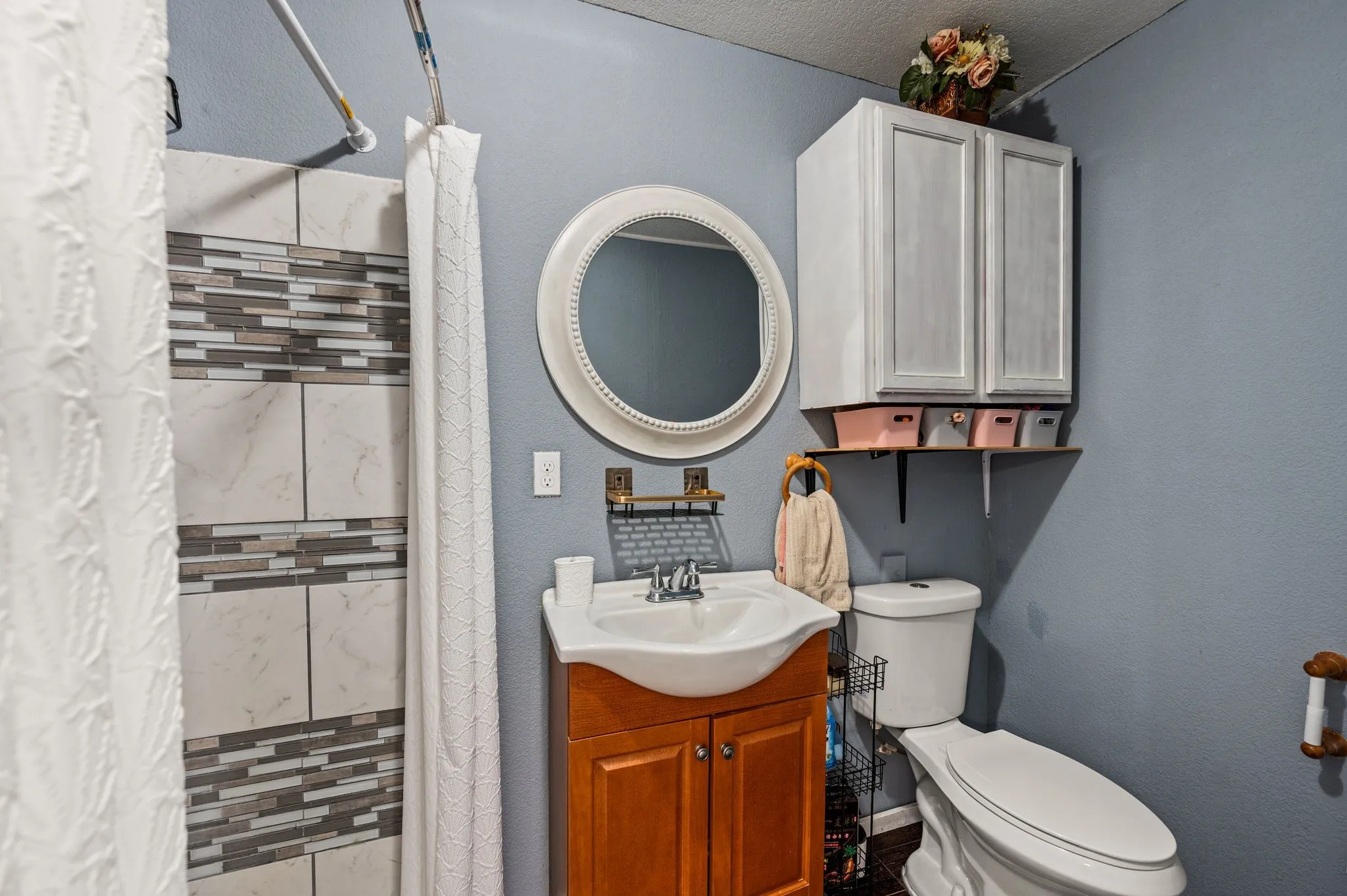 Shower with decorative tile inlay, circular vanity mirror, vanity with a white basin sink, and built-in wall cabinetry
