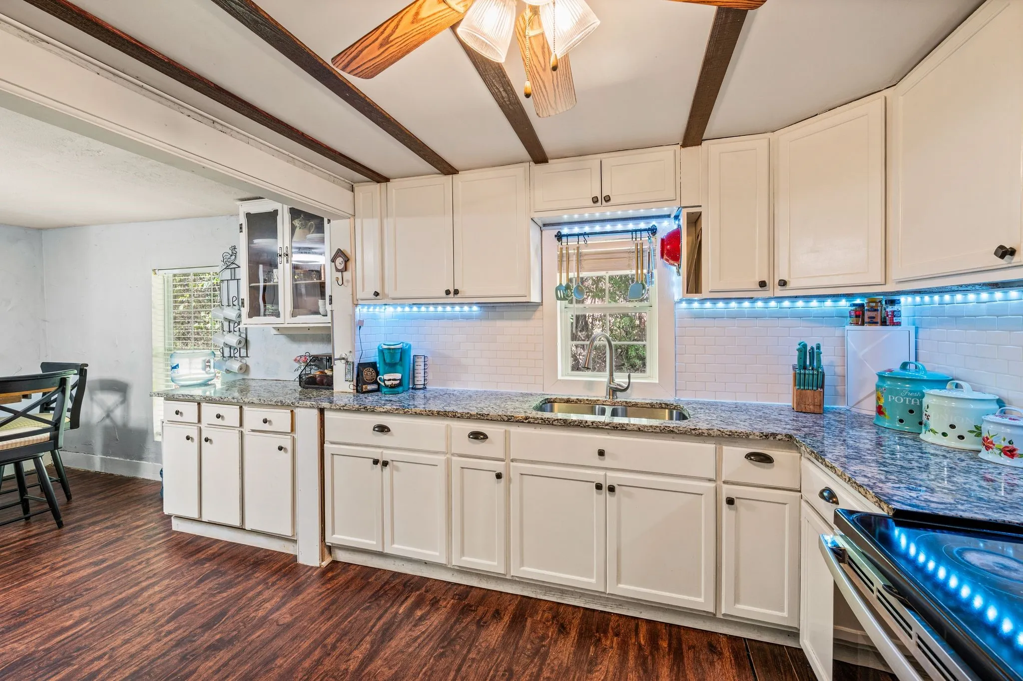 White cabinetry with dark hardware, stone countertops, stainless steel sink with a gooseneck faucet, white subway tile backsplash