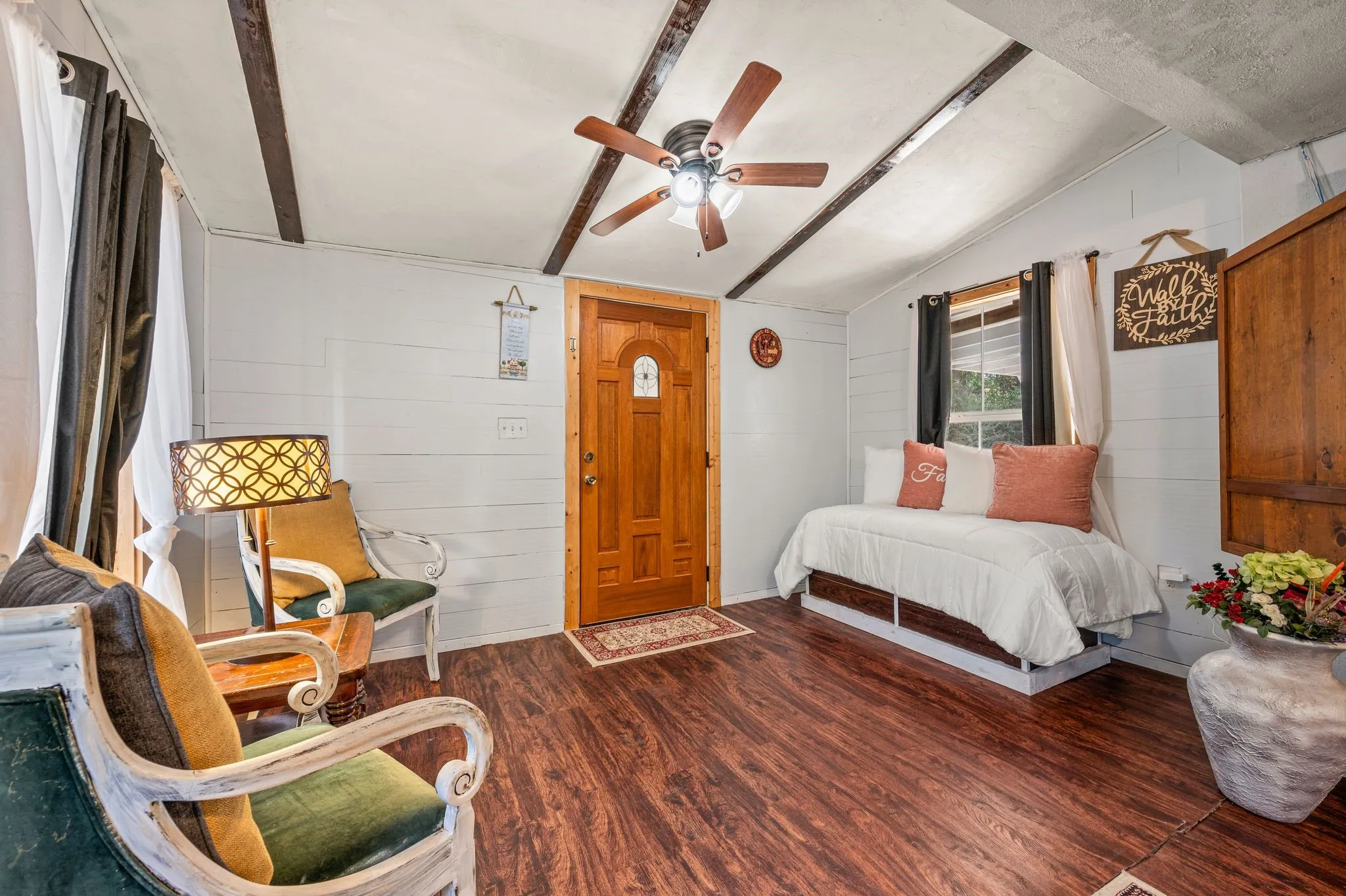  vaulted ceiling with exposed beams, wood-panel accent wall, wood-paneled door, and ceiling fan with integrated lighting