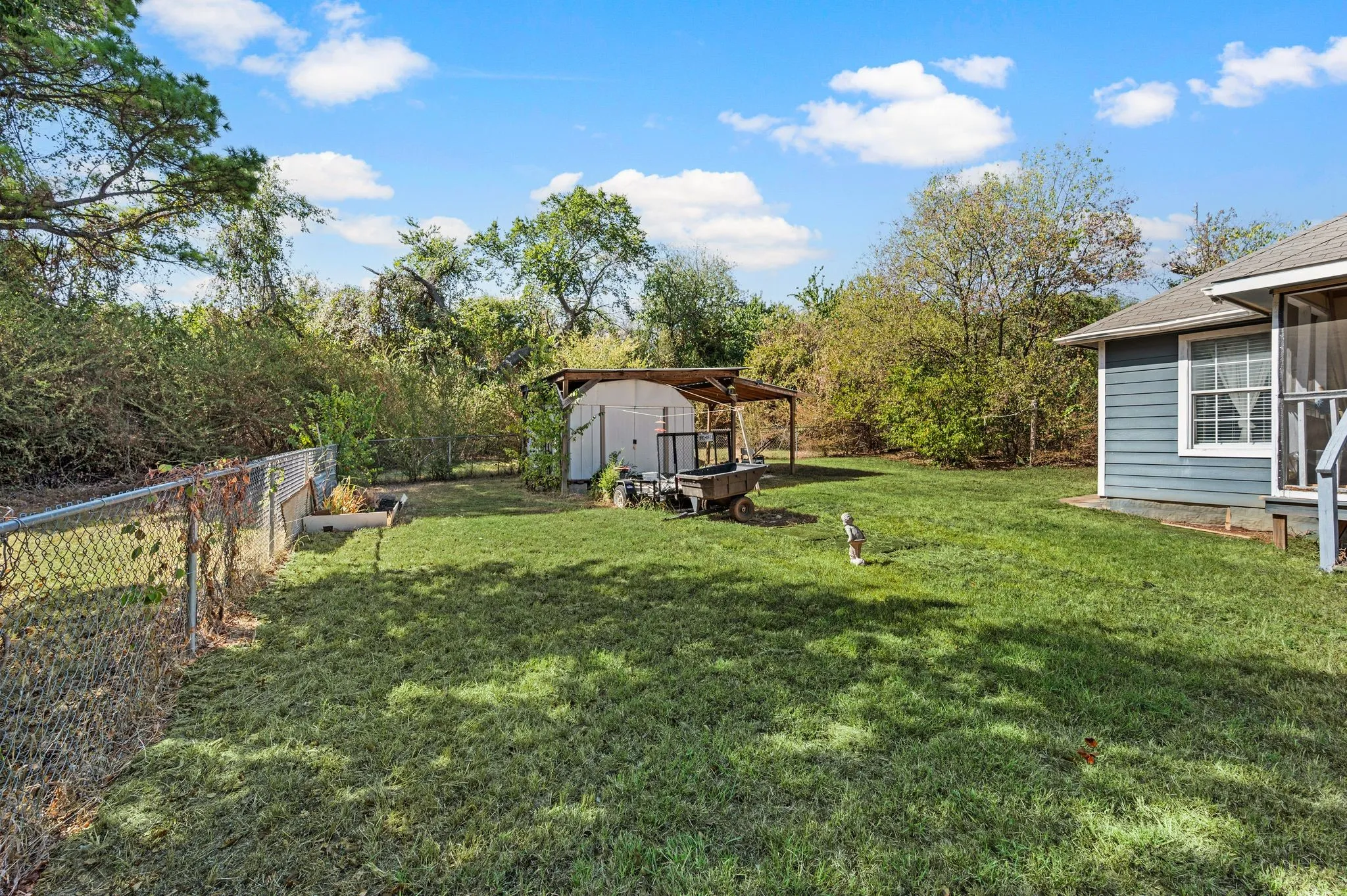 Expansive backyard featuring a green lawn, chain link fencing, a storage shed, and a covered patio structure