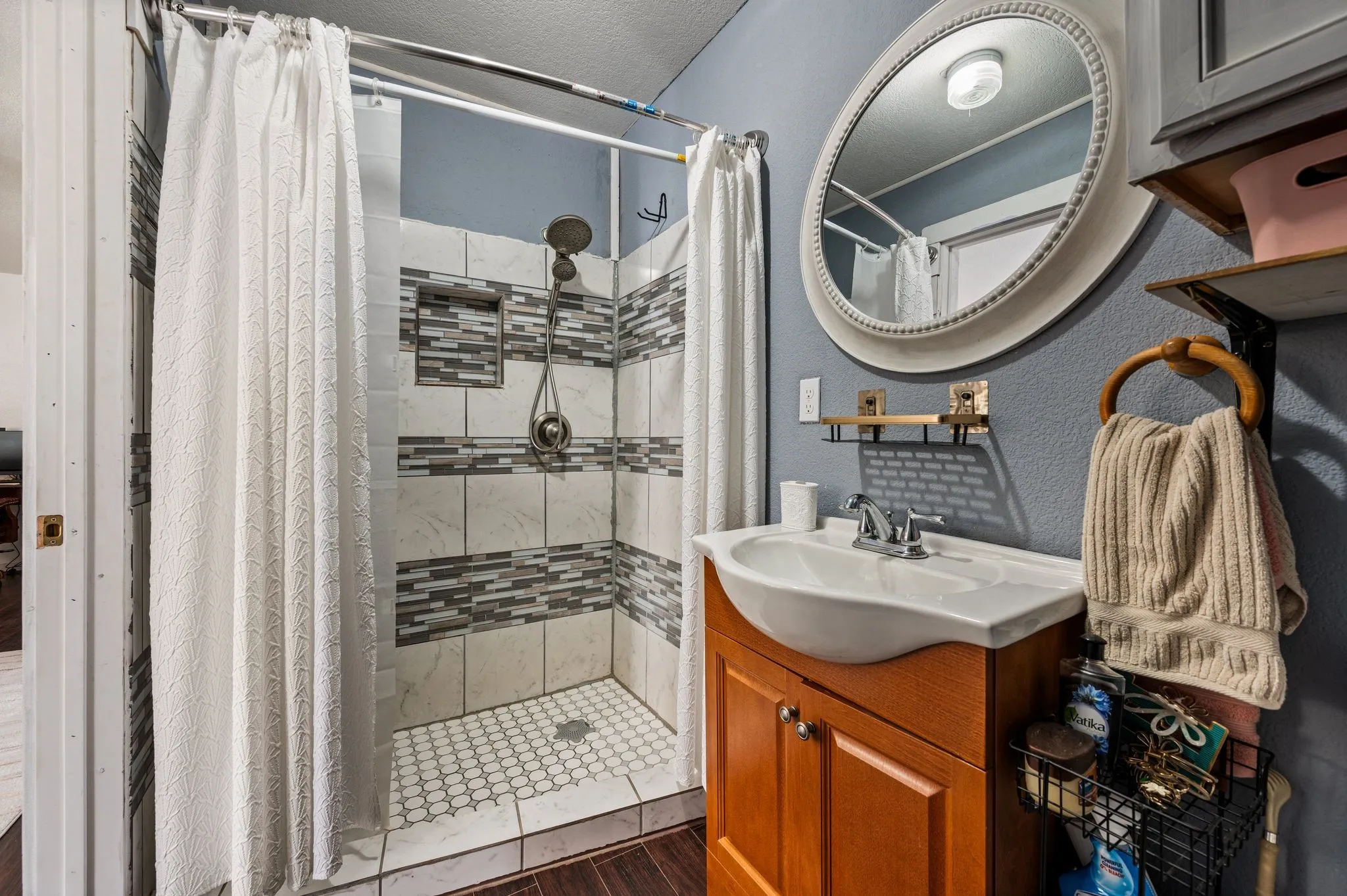 Tiled shower with mosaic accents and an integrated niche, complemented by a vanity with a drop-in sink and an oval mirror