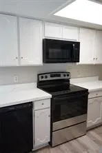 Kitchen featuring white cabinetry, white countertops, built-in microwave, electric range, and wood-finish flooring