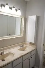 Dual basin vanity with integrated sinks, white cabinetry, wall-mounted storage cabinet, and overhead lighting fixture