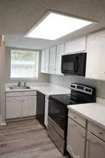 Kitchen featuring white cabinetry, light-toned countertops, a stainless steel dishwasher, a black range, and a black built-in microwave