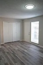 Wood-finish flooring with a neutral color palette, featuring a built-in closet with bi-fold doors, and a flush-mount ceiling light fixture