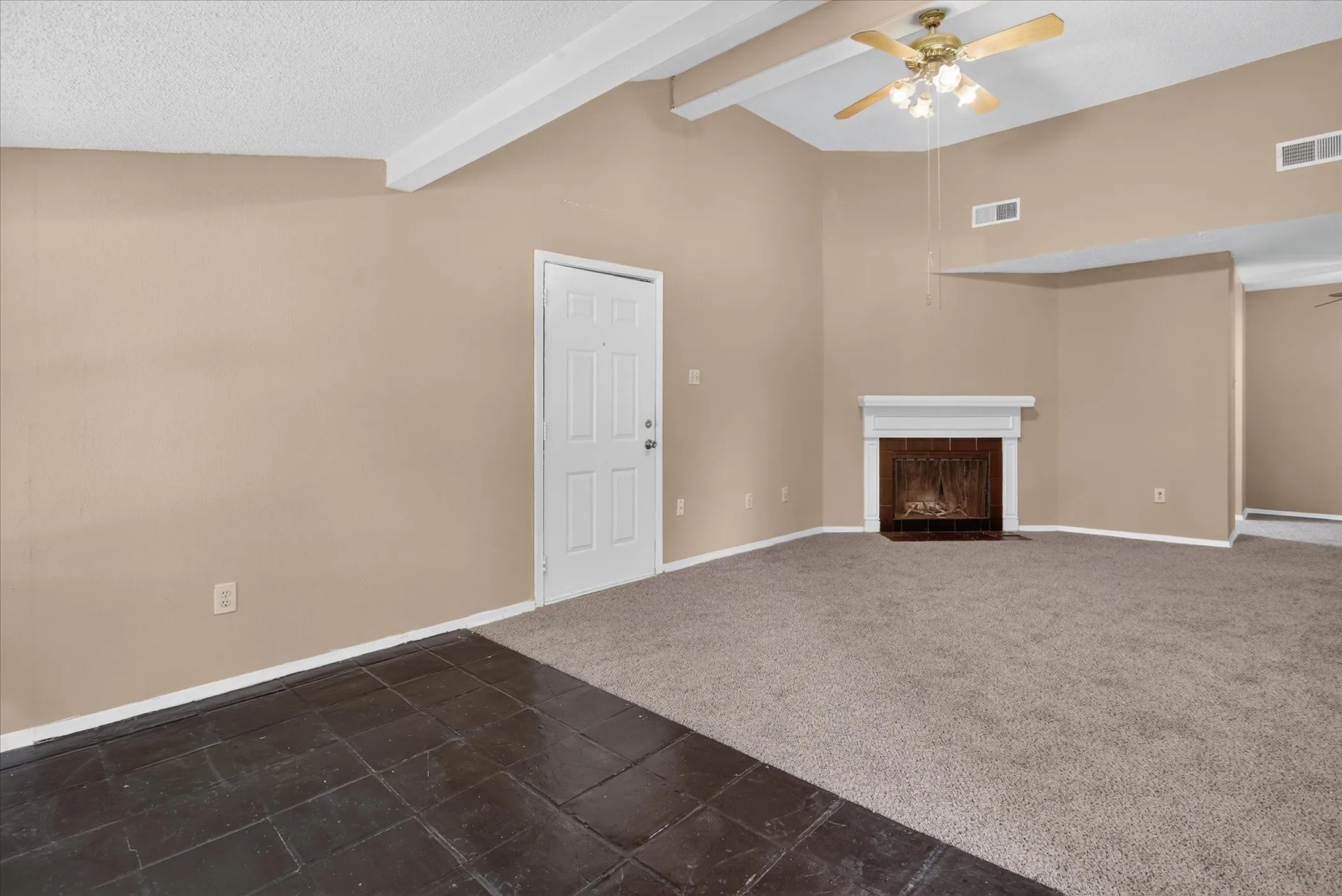 Vaulted ceiling with exposed beams, ceiling fan light fixture, white mantel over fireplace, mixed flooring with carpet and dark tile, and paneled interior door