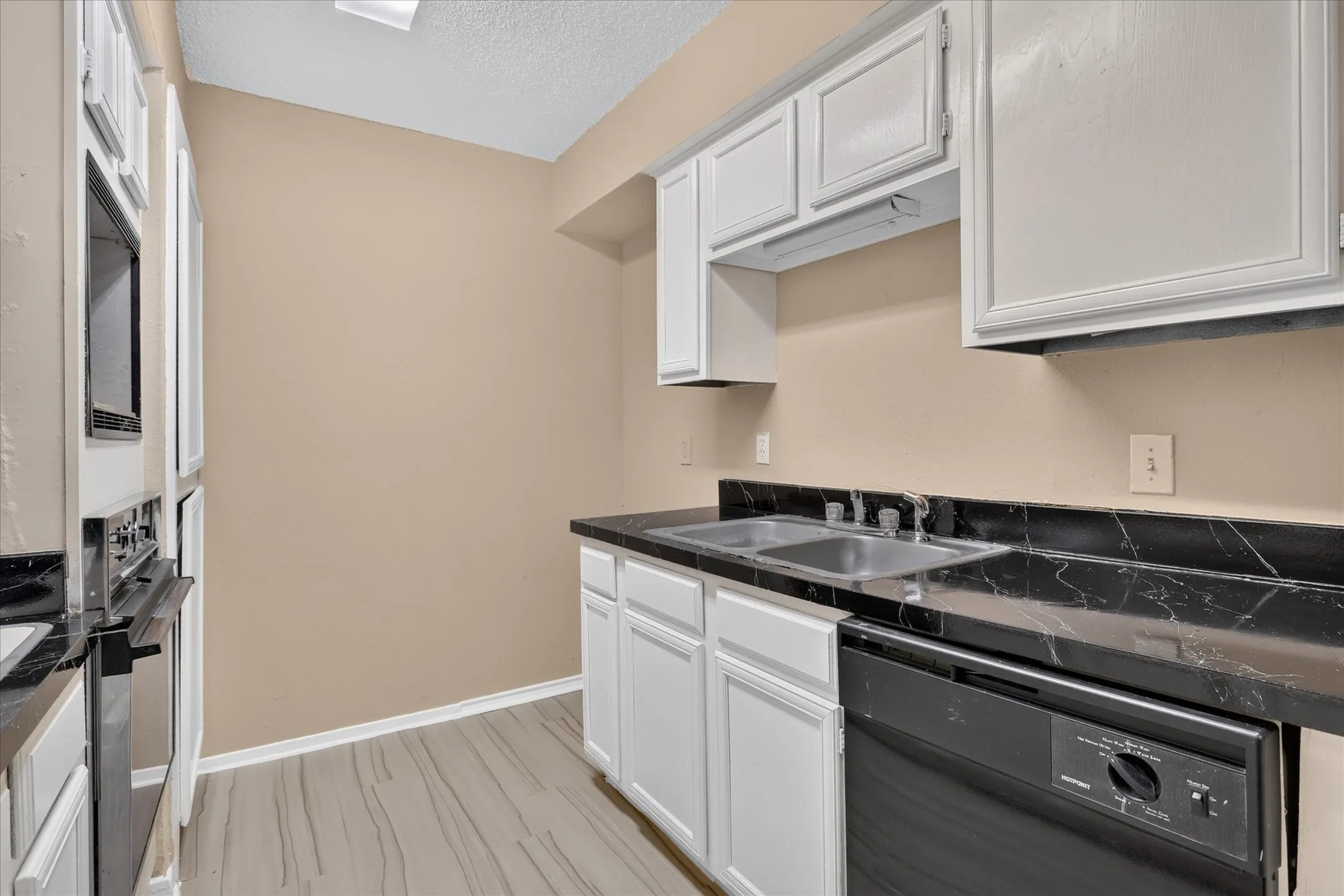 Kitchen featuring wood-finish flooring, white cabinetry, a double basin sink, black countertops, and a built-in oven and microwave