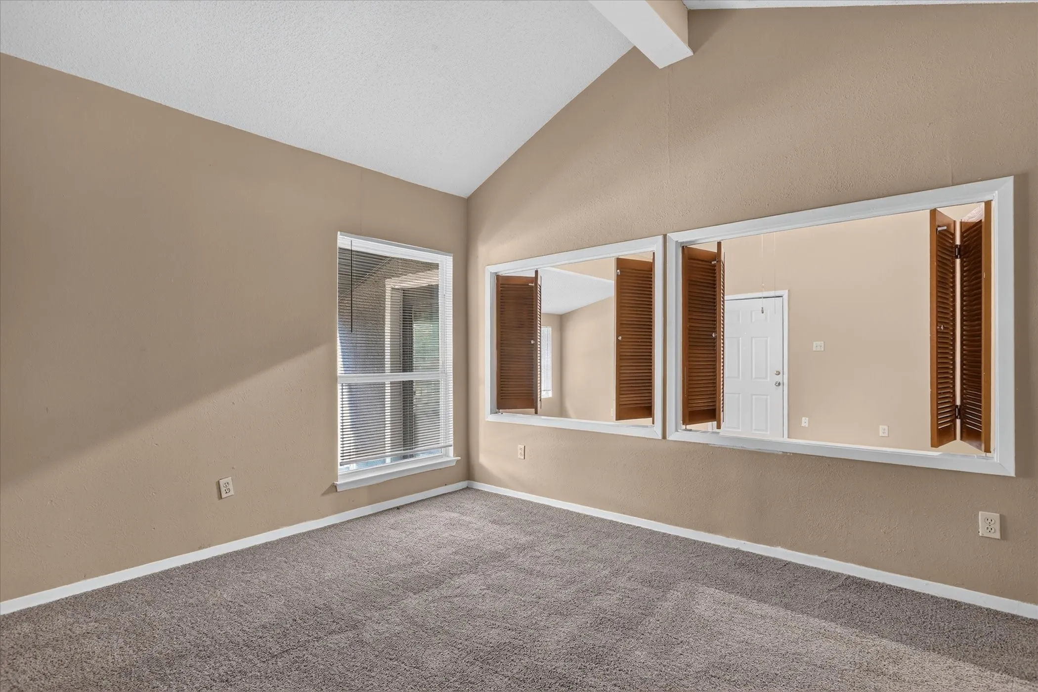 Vaulted ceiling with exposed beam, wall-to-wall carpeting, and a window with exterior visibility