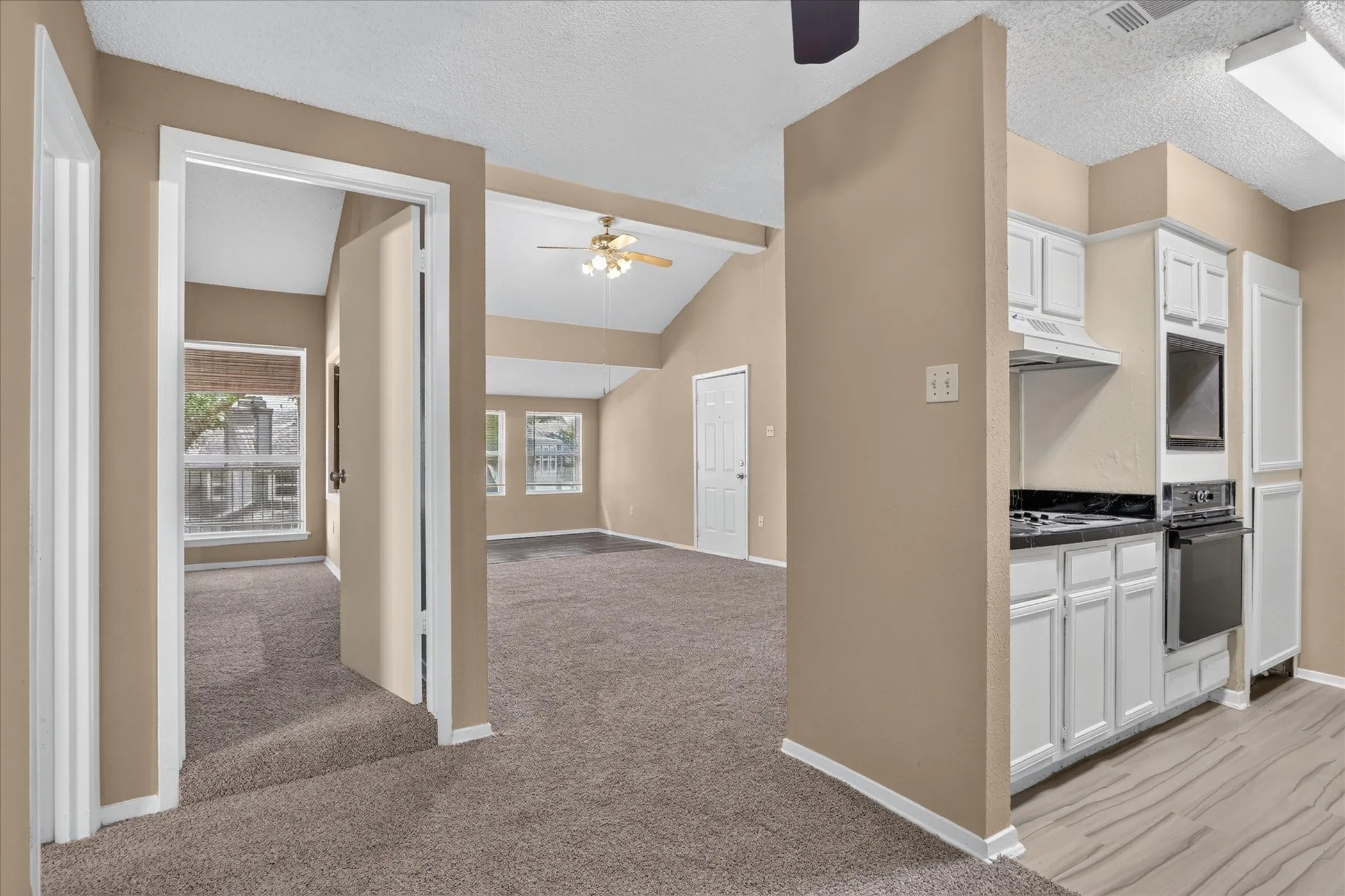Vaulted ceilings, a ceiling fan, white kitchen cabinetry, dark countertops, and wood-finish flooring