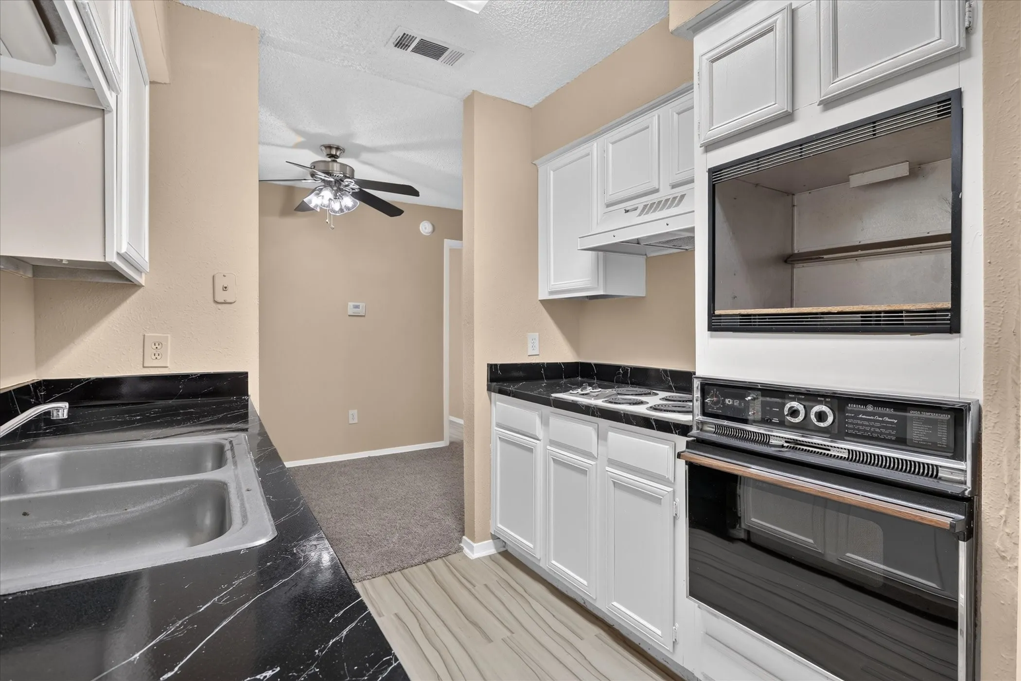 Kitchen featuring white cabinetry, black stone-finish countertops, stainless steel sink, and built-in double oven