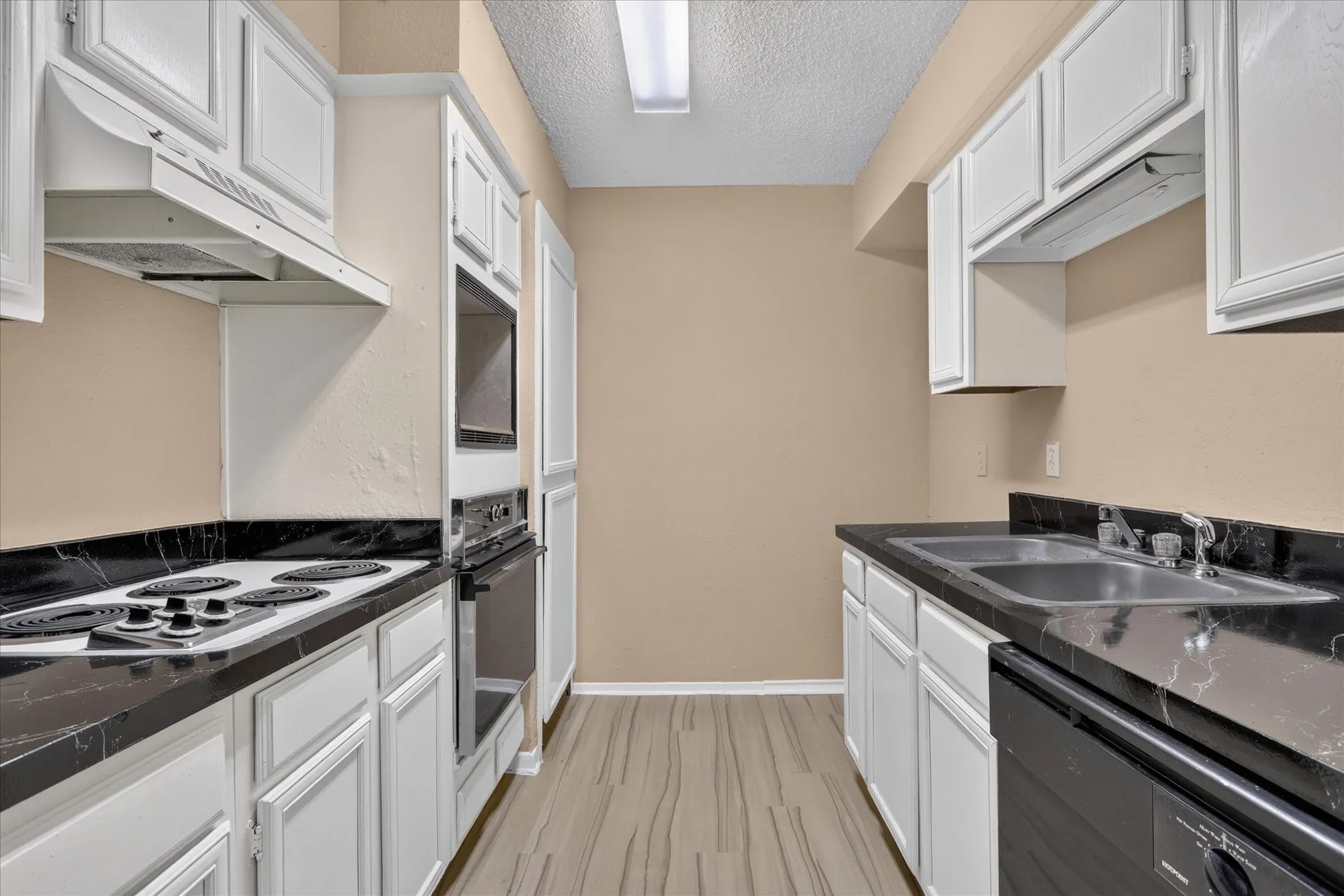 White cabinetry, black countertops, wood-finish flooring, built-in oven, and dual basin sink