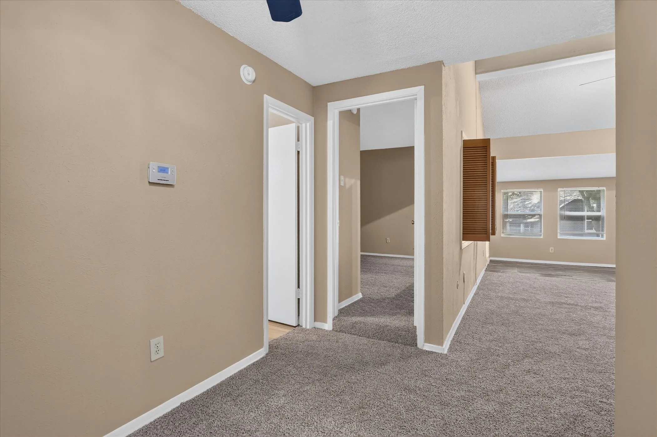 Vaulted ceiling, multiple windows, textured tan walls, white trim, and gray carpet flooring