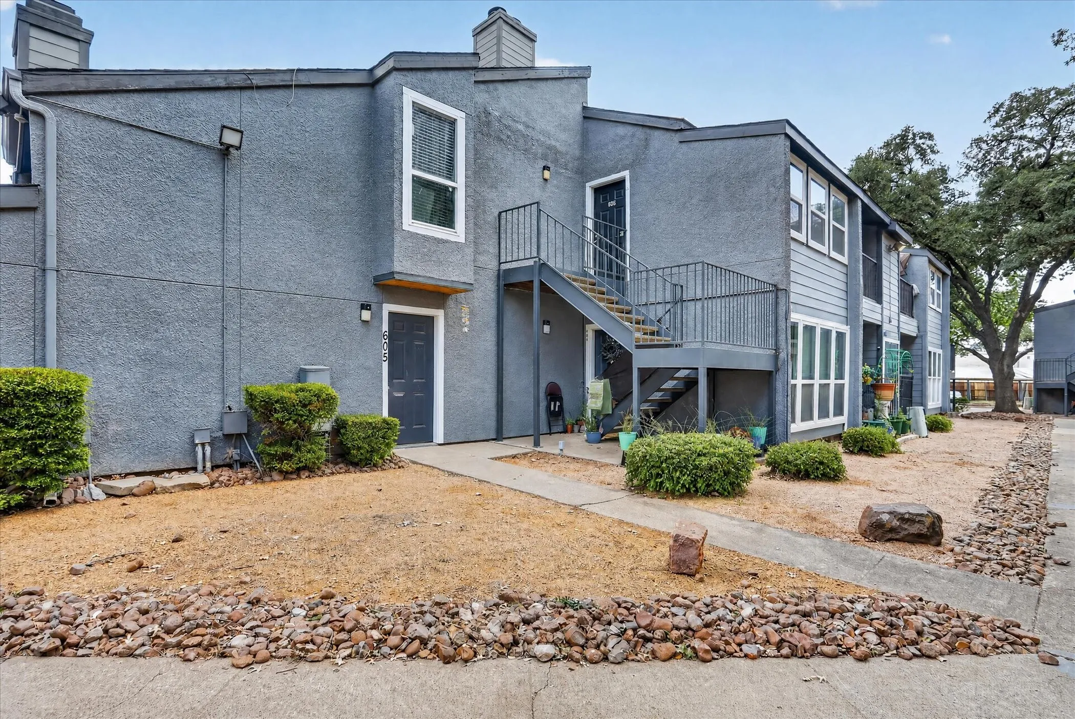 Multi-unit residential building featuring stucco and siding exteriors, exterior staircases, and mature trees
