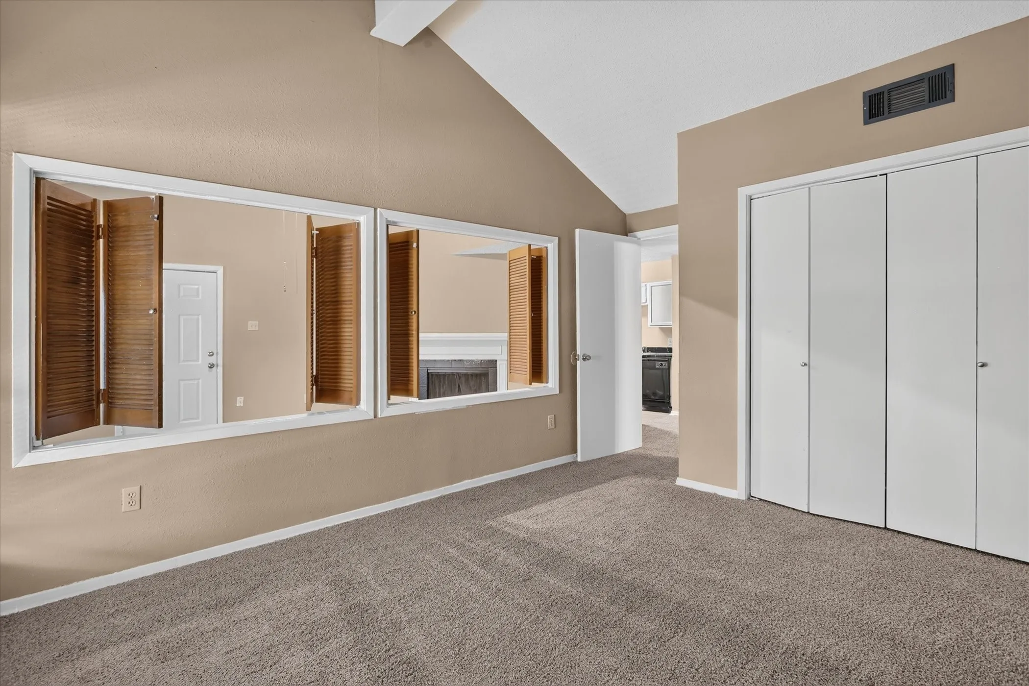 Vaulted ceiling, neutral tone walls, carpeted flooring, bi-fold closet doors, and interior shutters