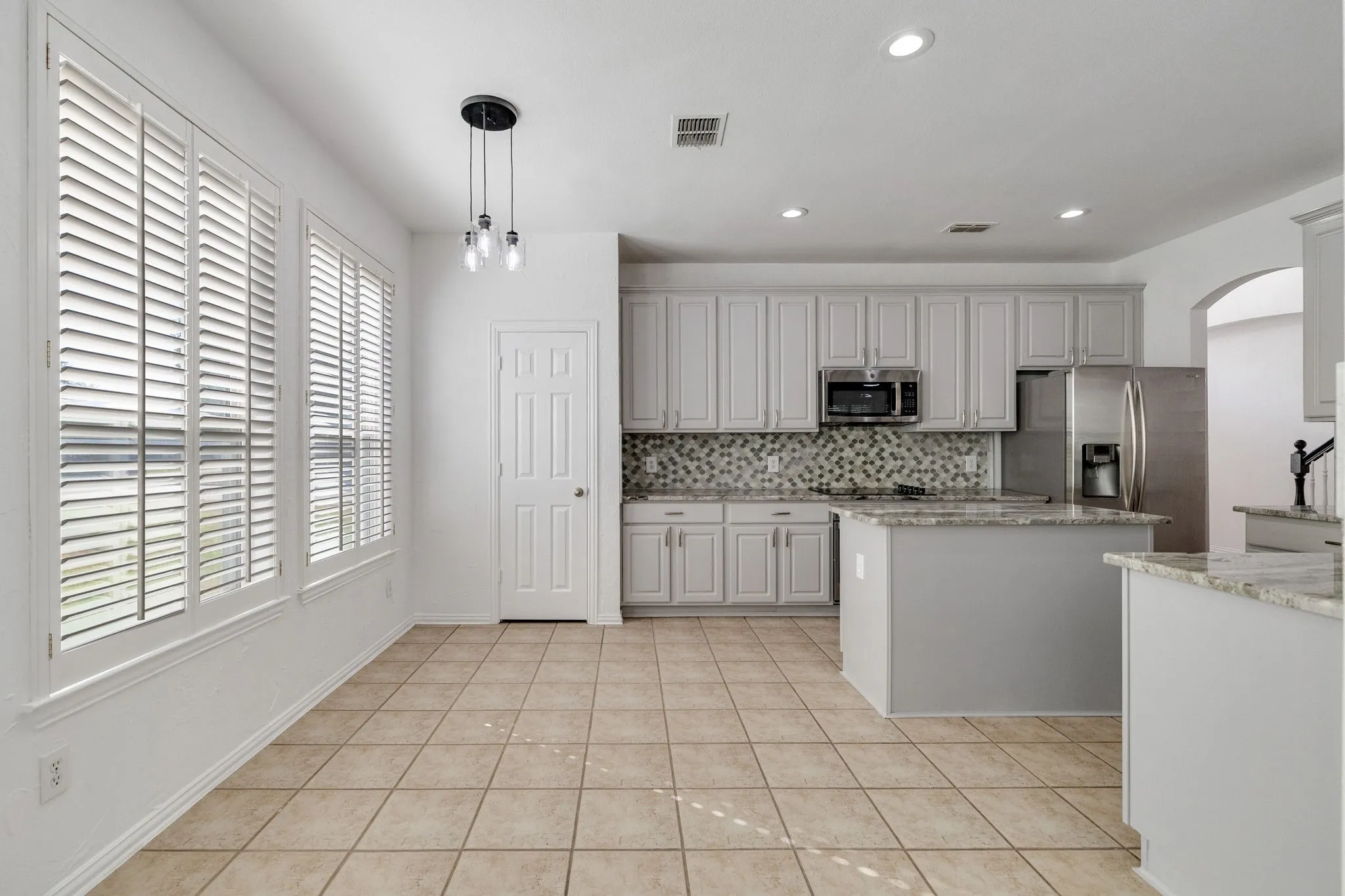 Kitchen featuring white cabinetry, stainless steel appliances, granite countertops, tile flooring, and a decorative tile backsplash
