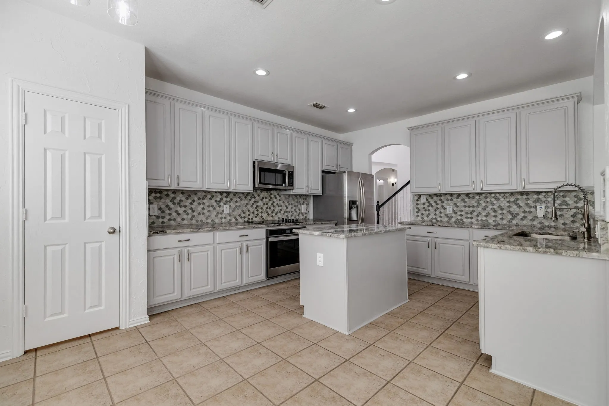 Kitchen featuring a central island, light-toned cabinetry, stainless steel appliances, patterned tile backsplash, and light-toned tile flooring