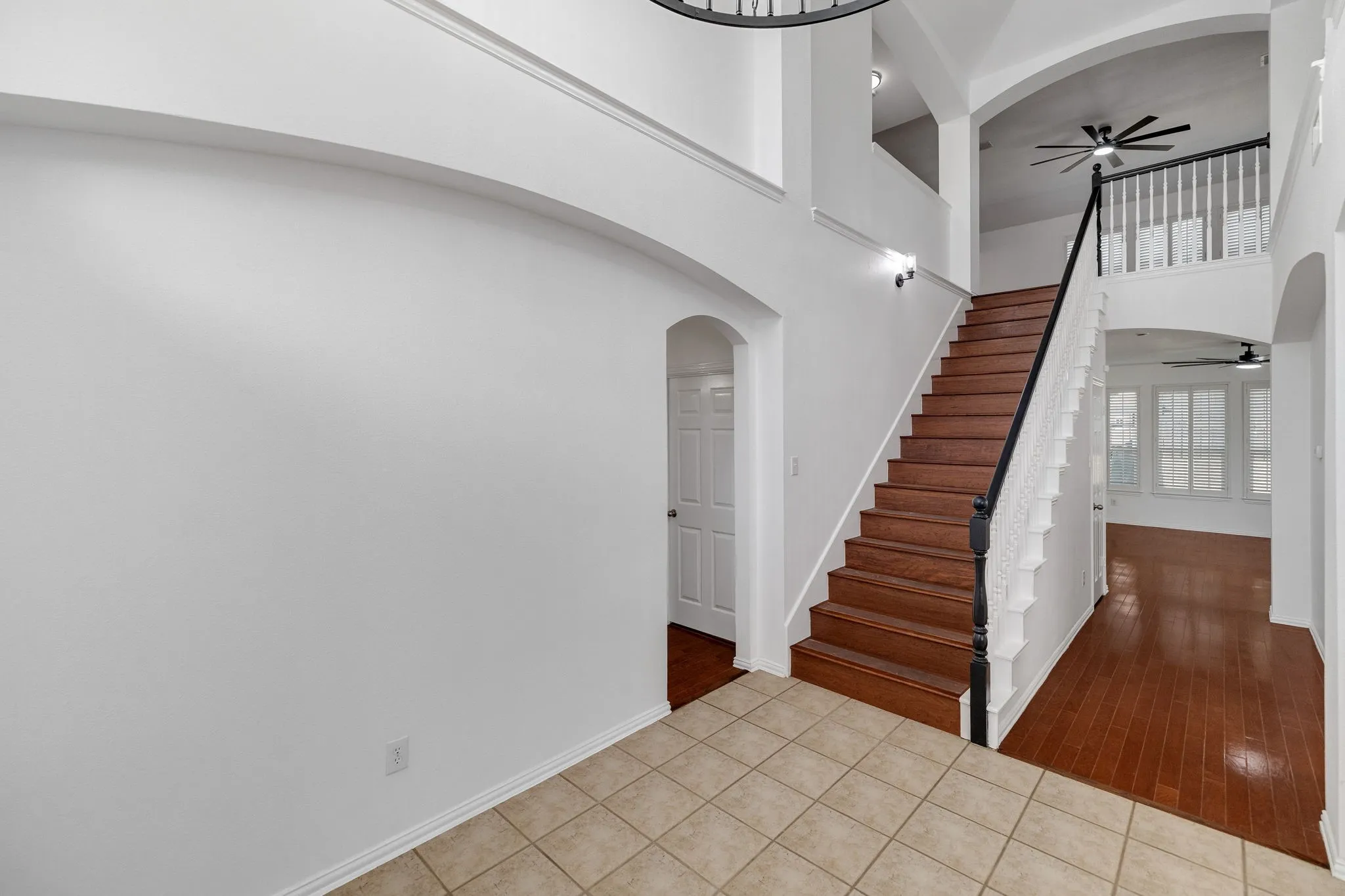 Tiled entry with wood-finish flooring, staircase with dark wood-finish handrail, and arched doorways