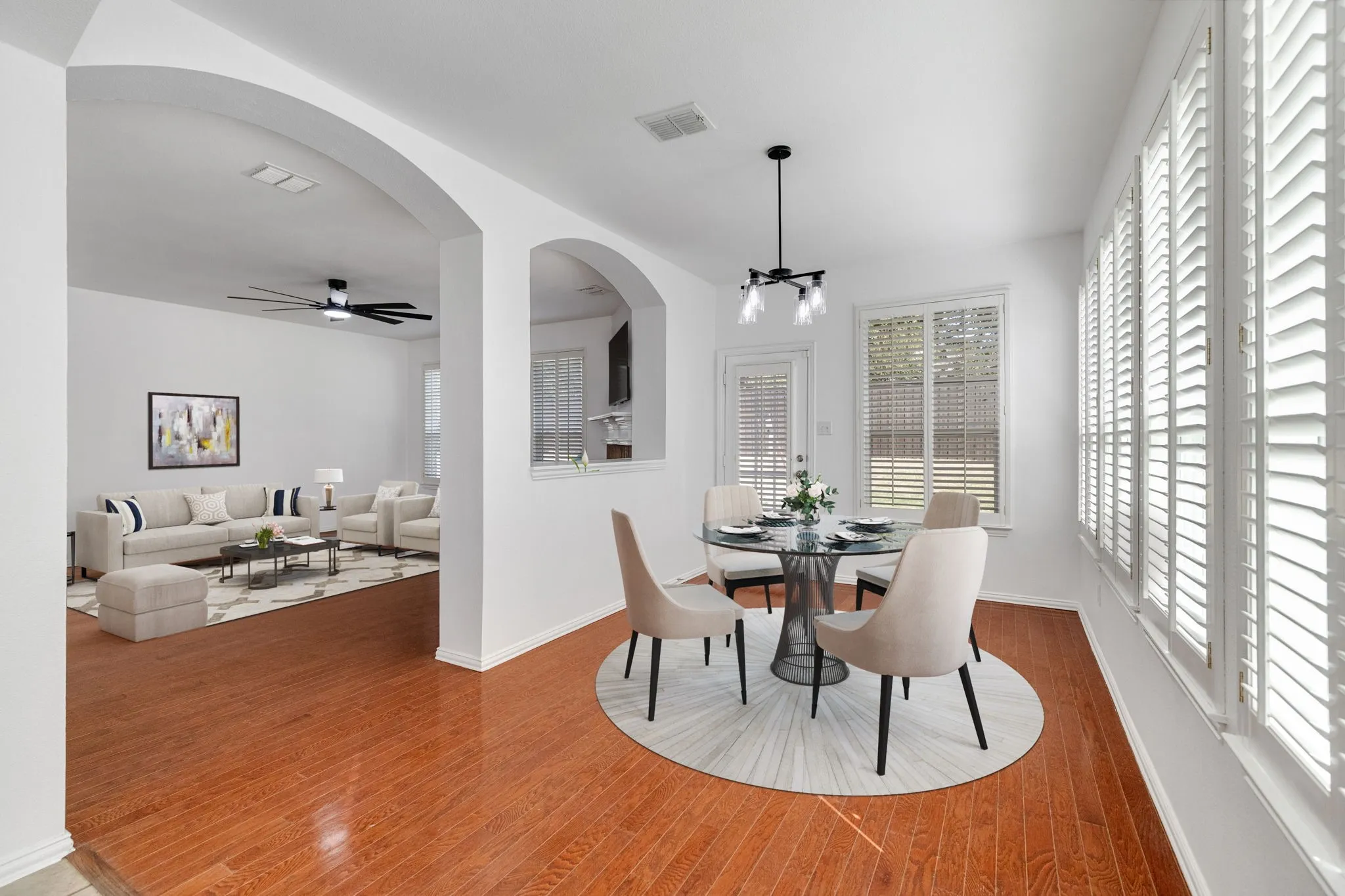 Arched doorways, wood-finish flooring, white plantation shutters, built-in ceiling fan, and a modern chandelier