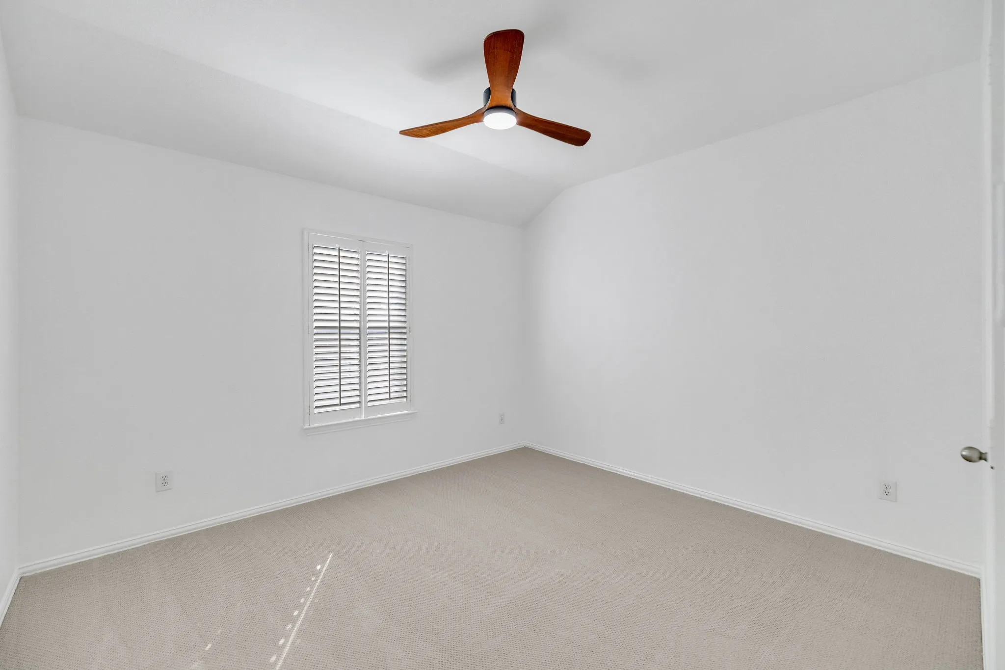 Carpeted flooring, white walls, window with plantation shutters, wood-finish ceiling fan with integrated lighting