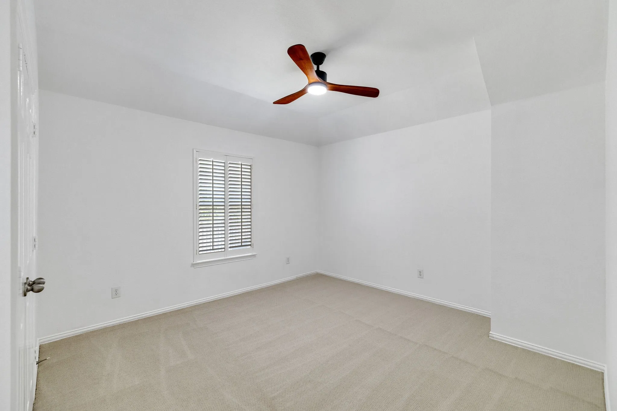 Recessed window with plantation shutters, neutral carpeting, and a ceiling fan with integrated lighting