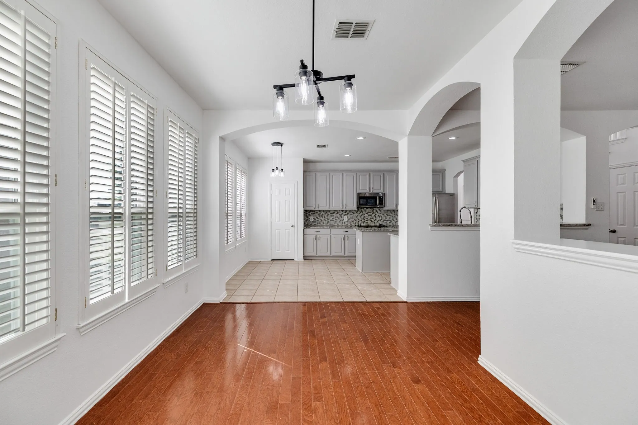 Hardwood-finish flooring, plantation shutters, arched pass-throughs, recessed lighting, and a modern chandelier