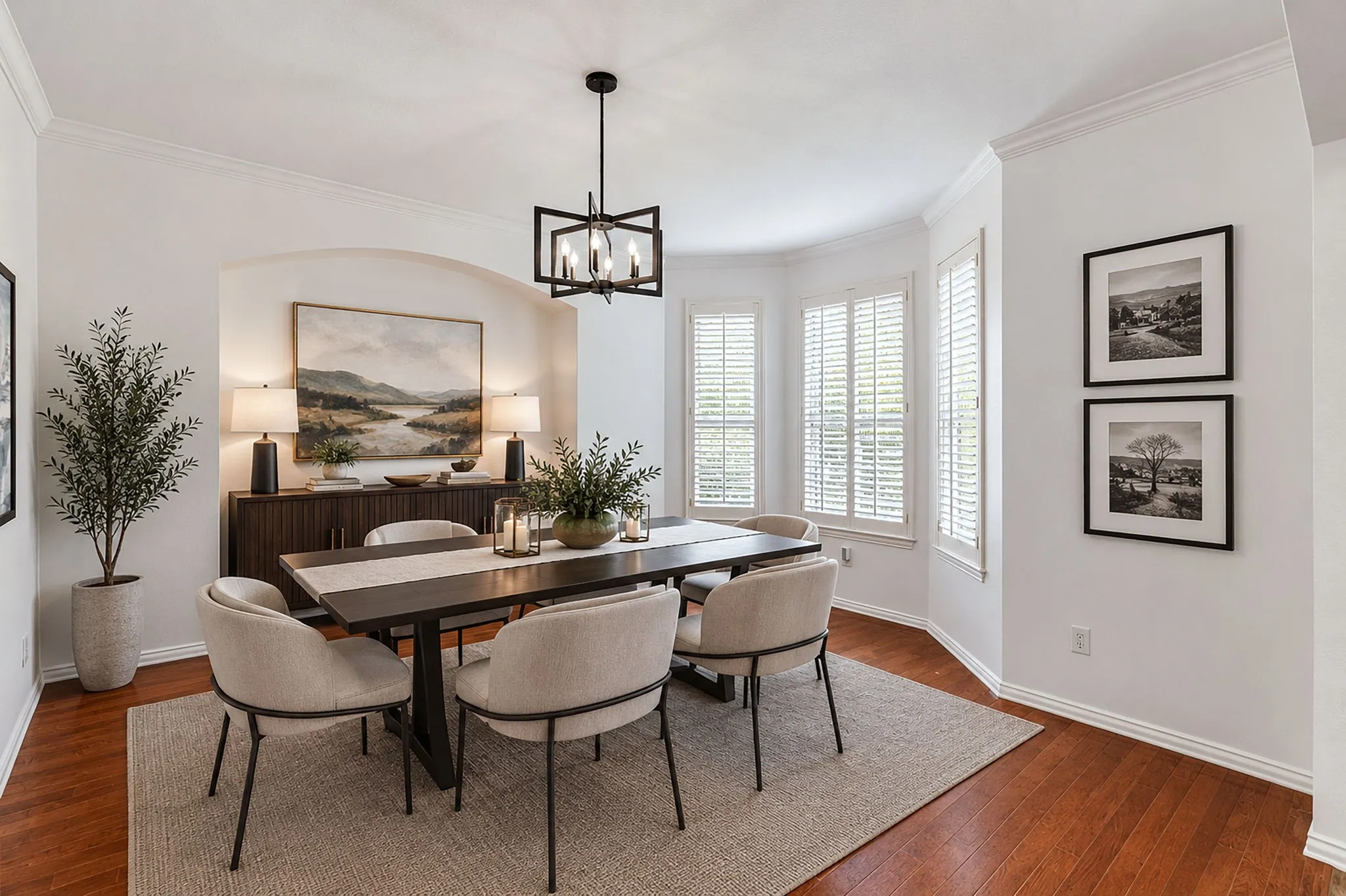 Hardwood flooring, arched wall niche, bay window with plantation shutters, crown molding, and a contemporary chandelier