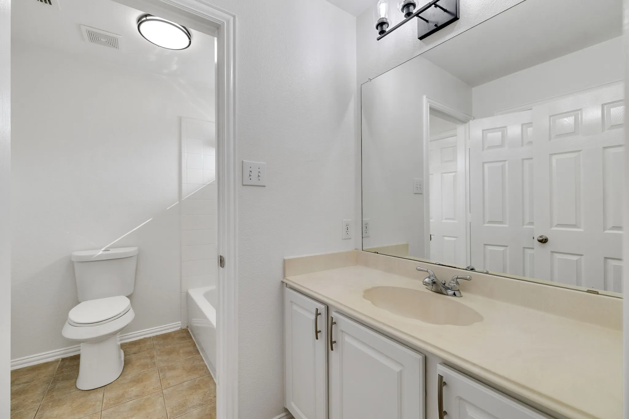 White vanity with cabinet storage, integrated sink, large wall-mounted mirror, and tile flooring