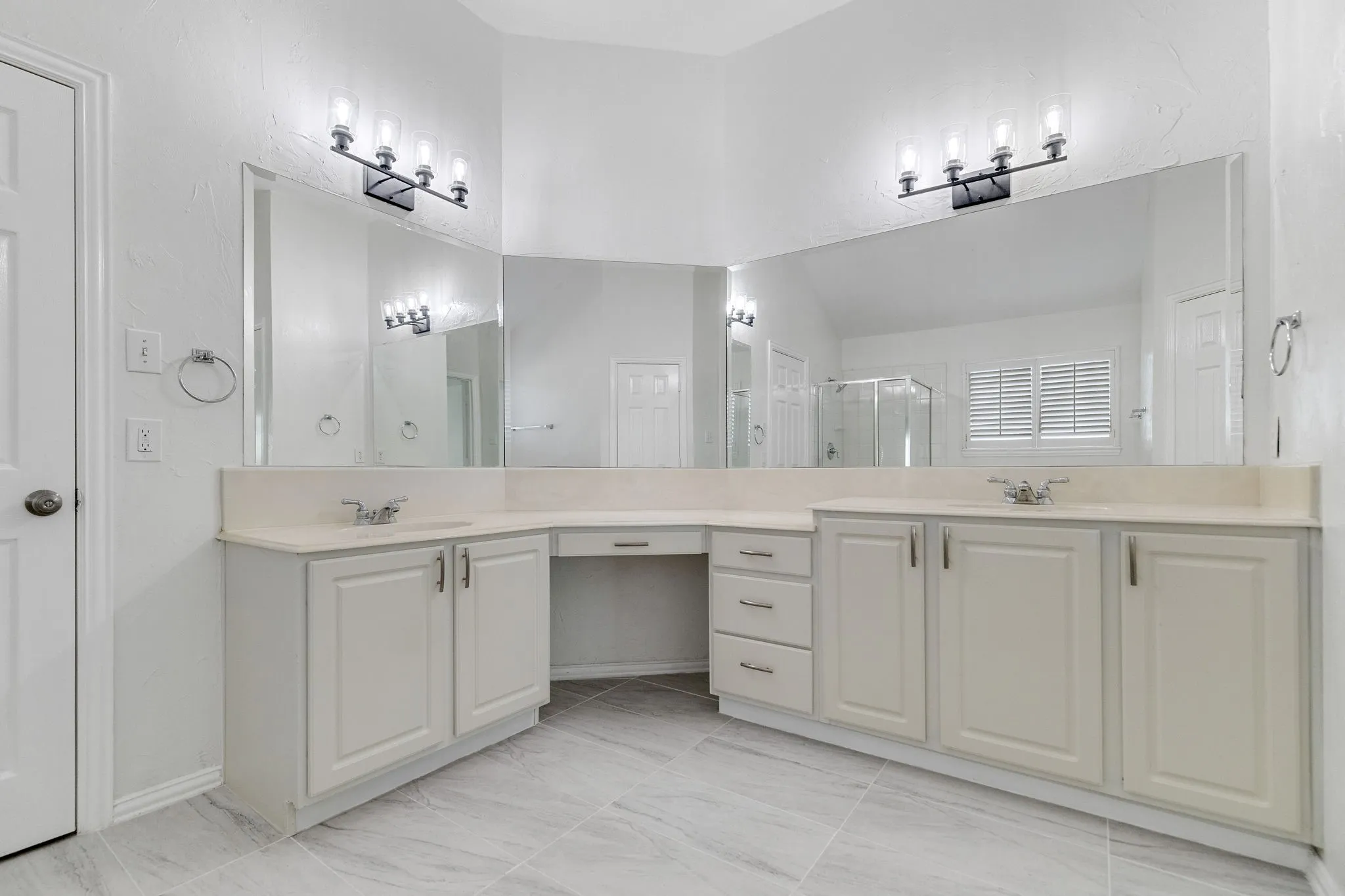 Dual vanity with light-toned countertops, white cabinetry, expansive mirrors, and decorative light fixtures