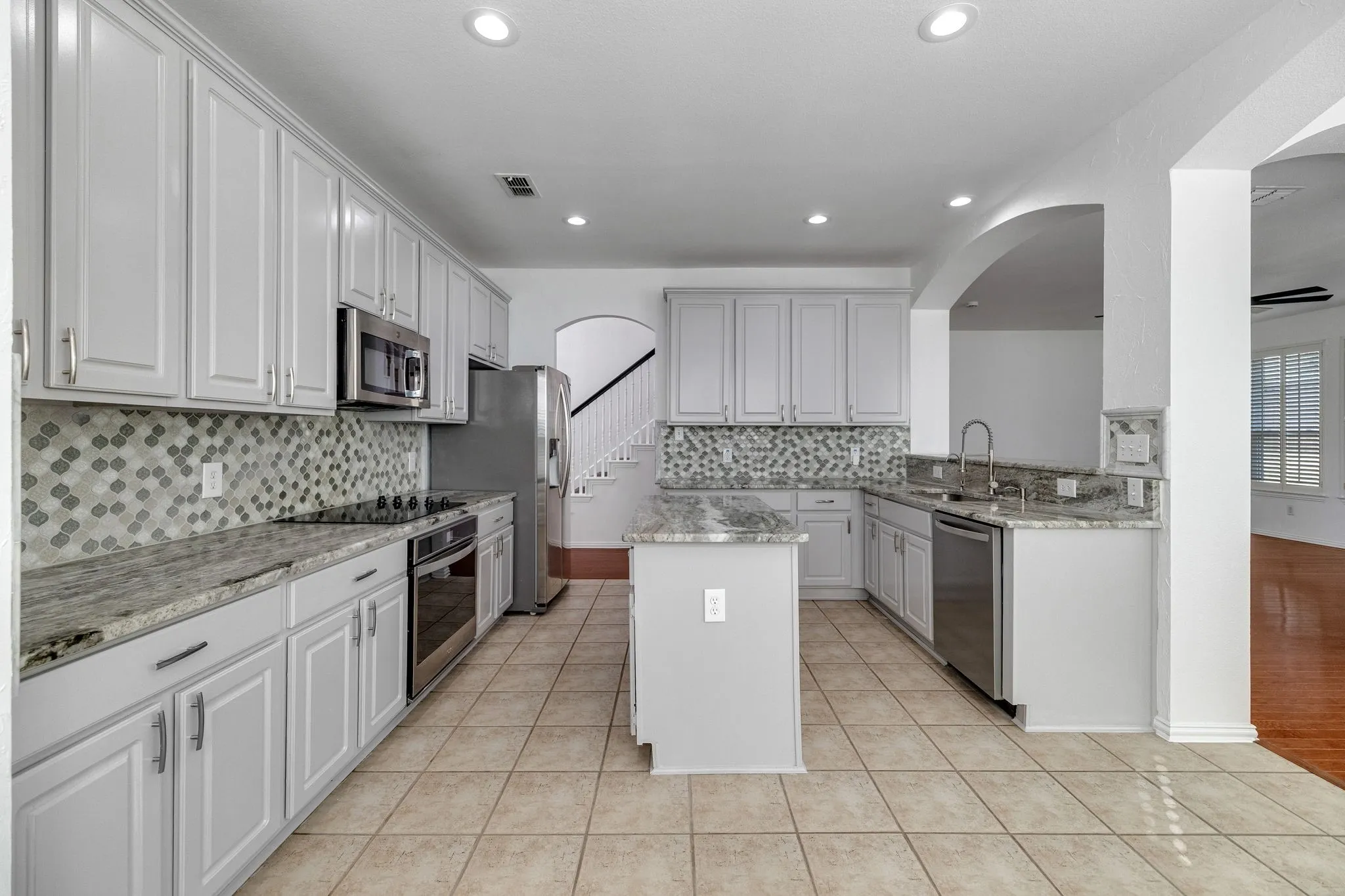Kitchen featuring light-toned cabinetry, light-toned countertops, stainless steel appliances, a mosaic tile backsplash, and ceramic tile flooring