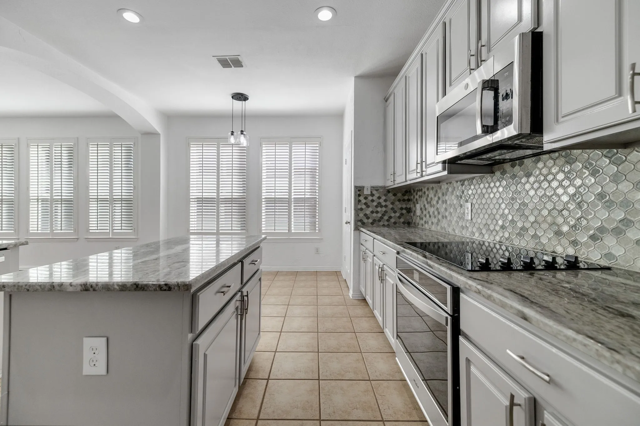 Kitchen featuring light-toned cabinetry, a stainless steel microwave, a built-in cooktop, and a distinct mosaic tile backsplash