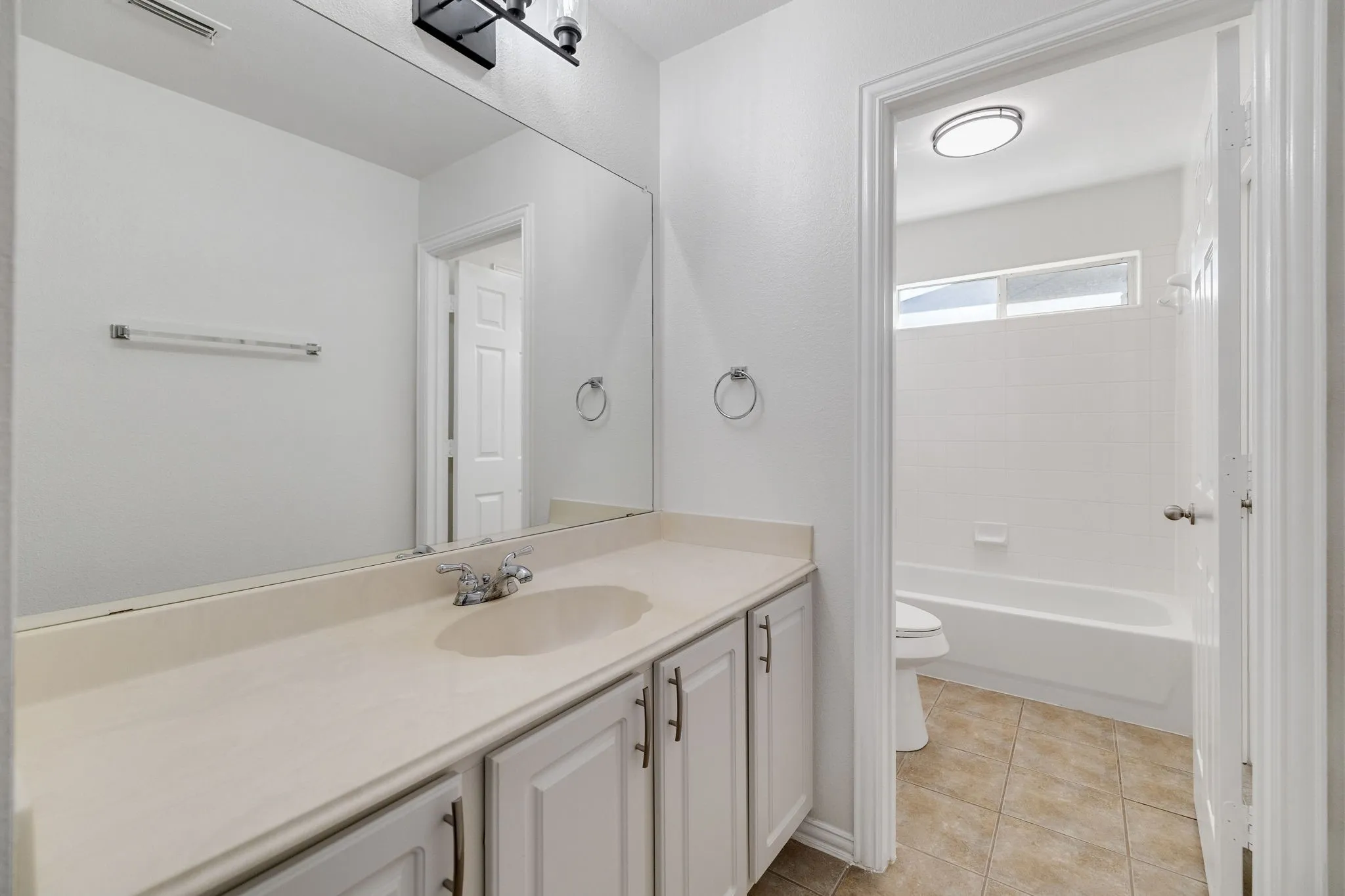 White paneled vanity with chrome hardware, an integrated sink, and an expansive wall mirror