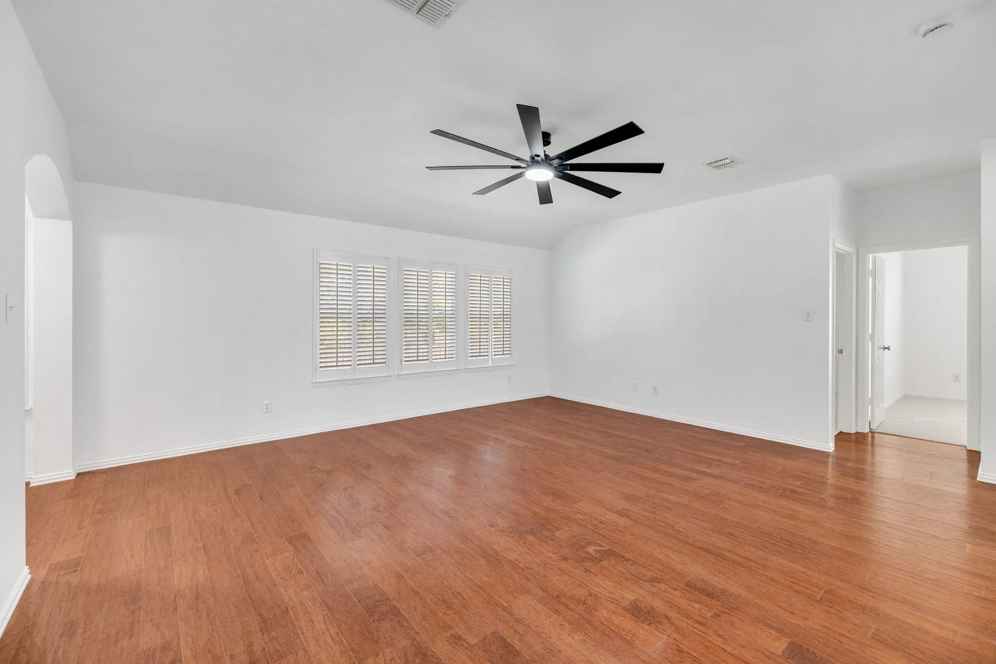 Vaulted ceiling with a contemporary ceiling fan, wood-finish flooring, and multiple windows with plantation shutters