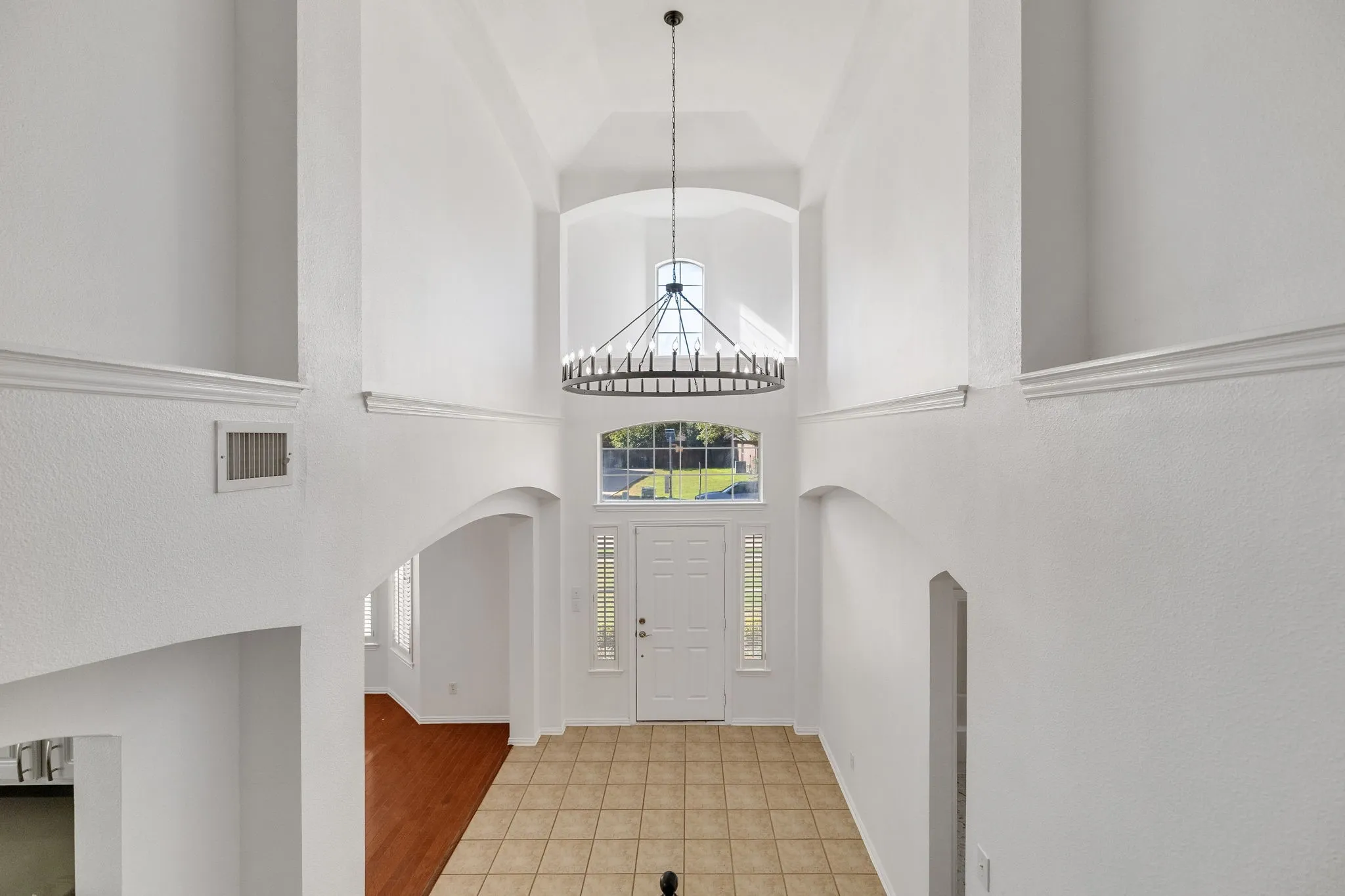 Two-story foyer with a vaulted ceiling, prominent chandelier, arched doorway, and tile flooring